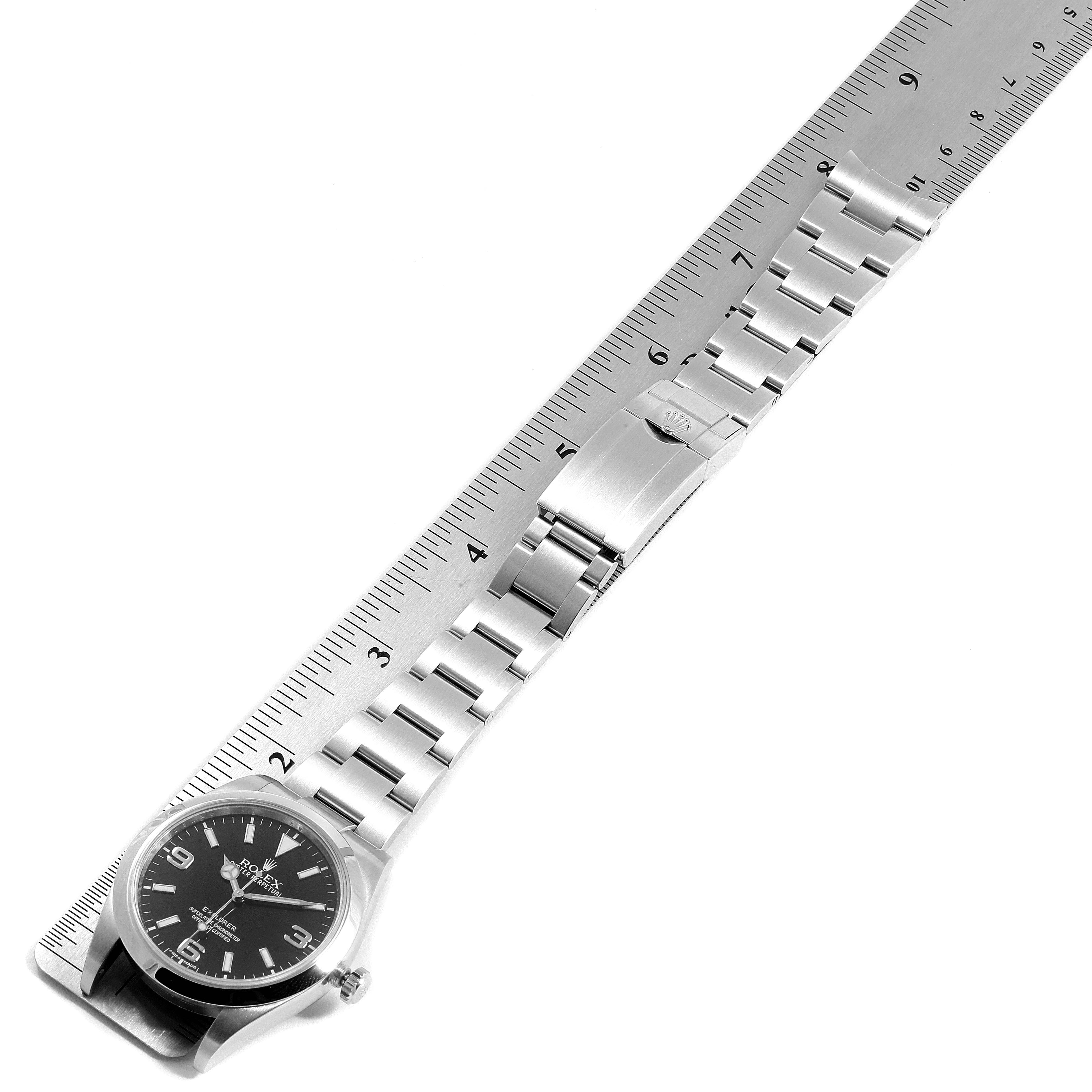 The image shows a Rolex Explorer 214270 Men
s Stainless Steel Black Dial 214270 Men
s Stainless Steel Black Dial watch laid flat with its face, bracelet, and clasp clearly visible, parallel to a measuring ruler.