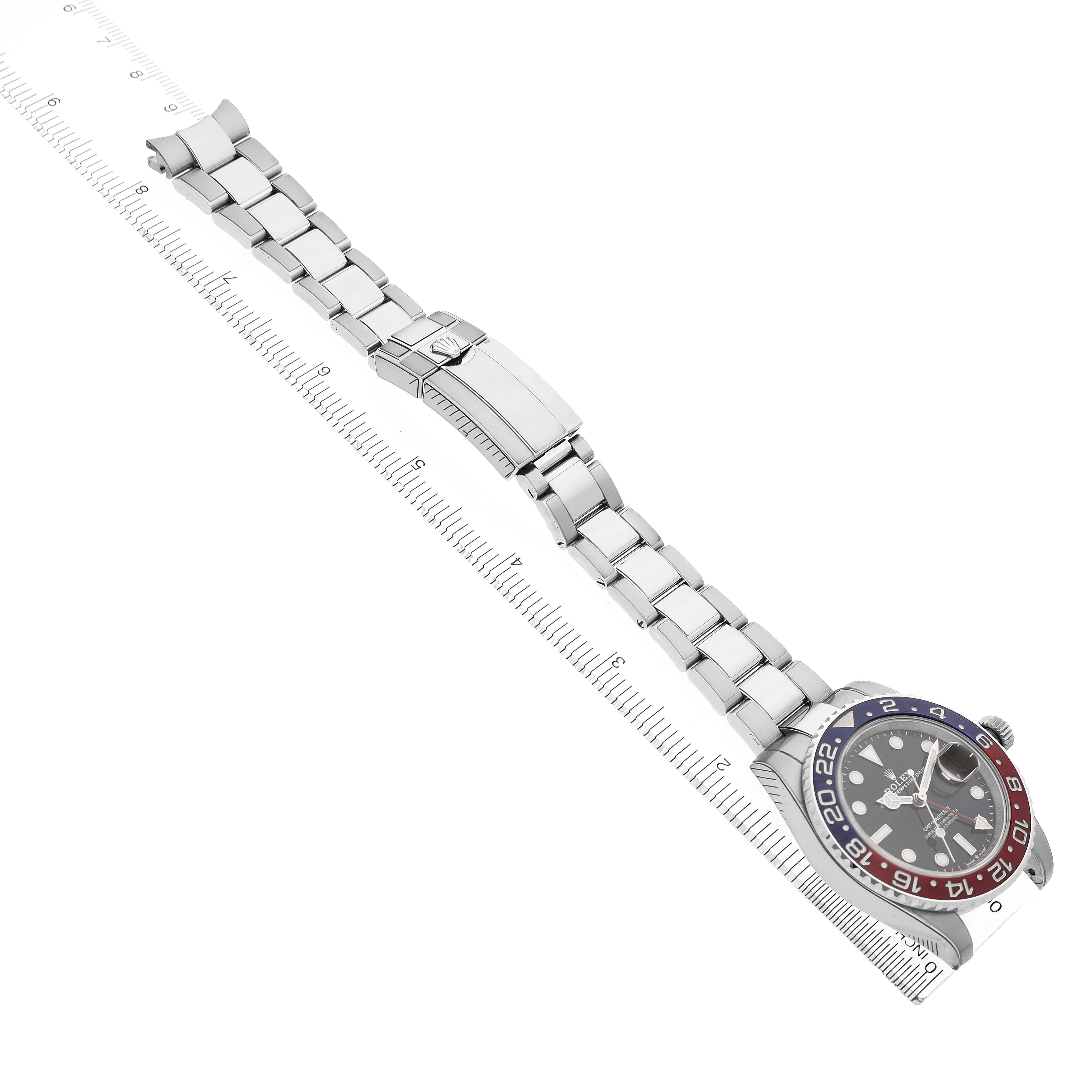 The Rolex GMT-Master 126710 Men's Stainless Steel Black Dial is shown from a top-down angle, highlighting the watch face, bezel, and full bracelet laid along a ruler.