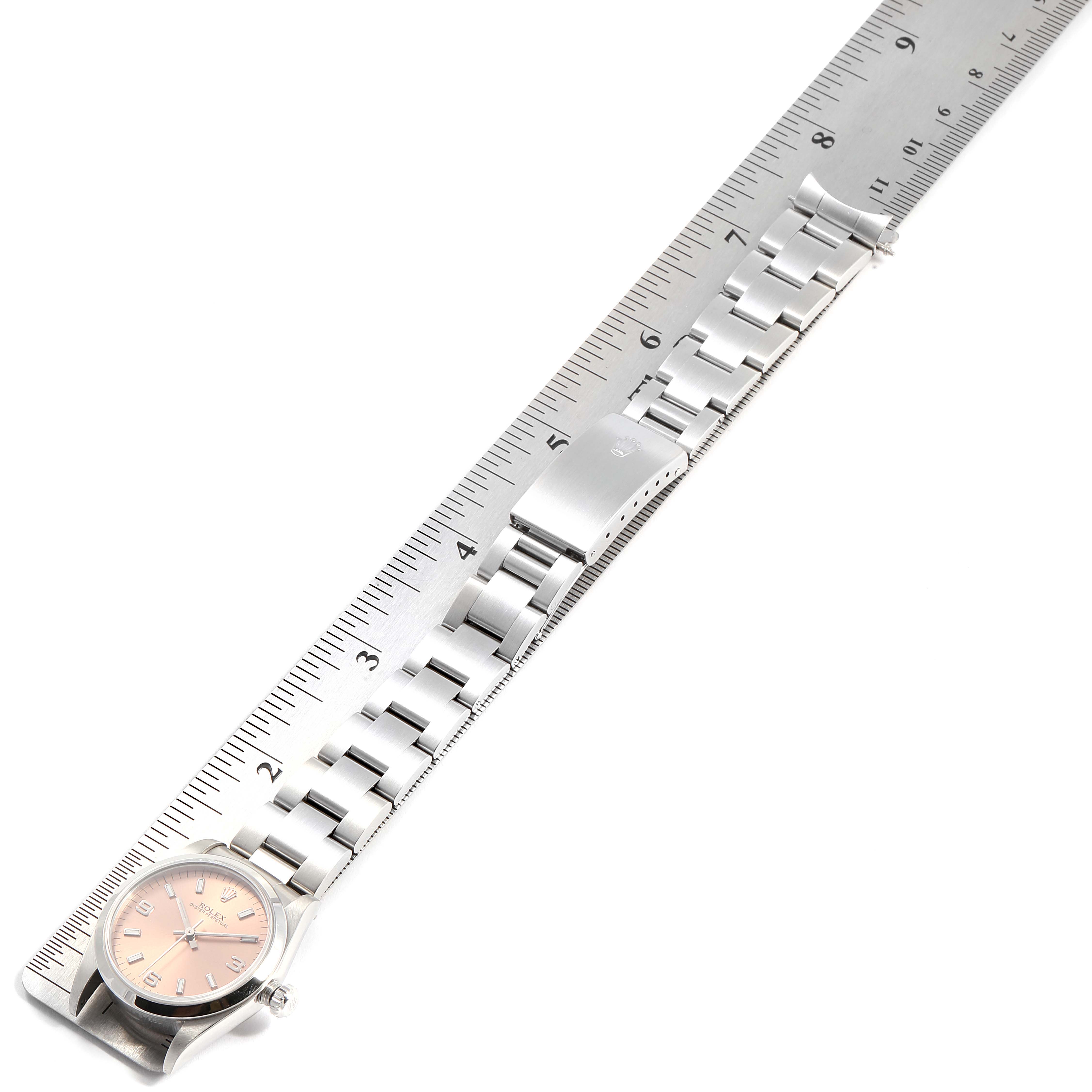 The image shows a Rolex Mid-Size 77080 Women
s Stainless Steel Pink Dial 77080 Women
s Stainless Steel Pink Dial watch laid flat next to a ruler, highlighting its face and full bracelet.