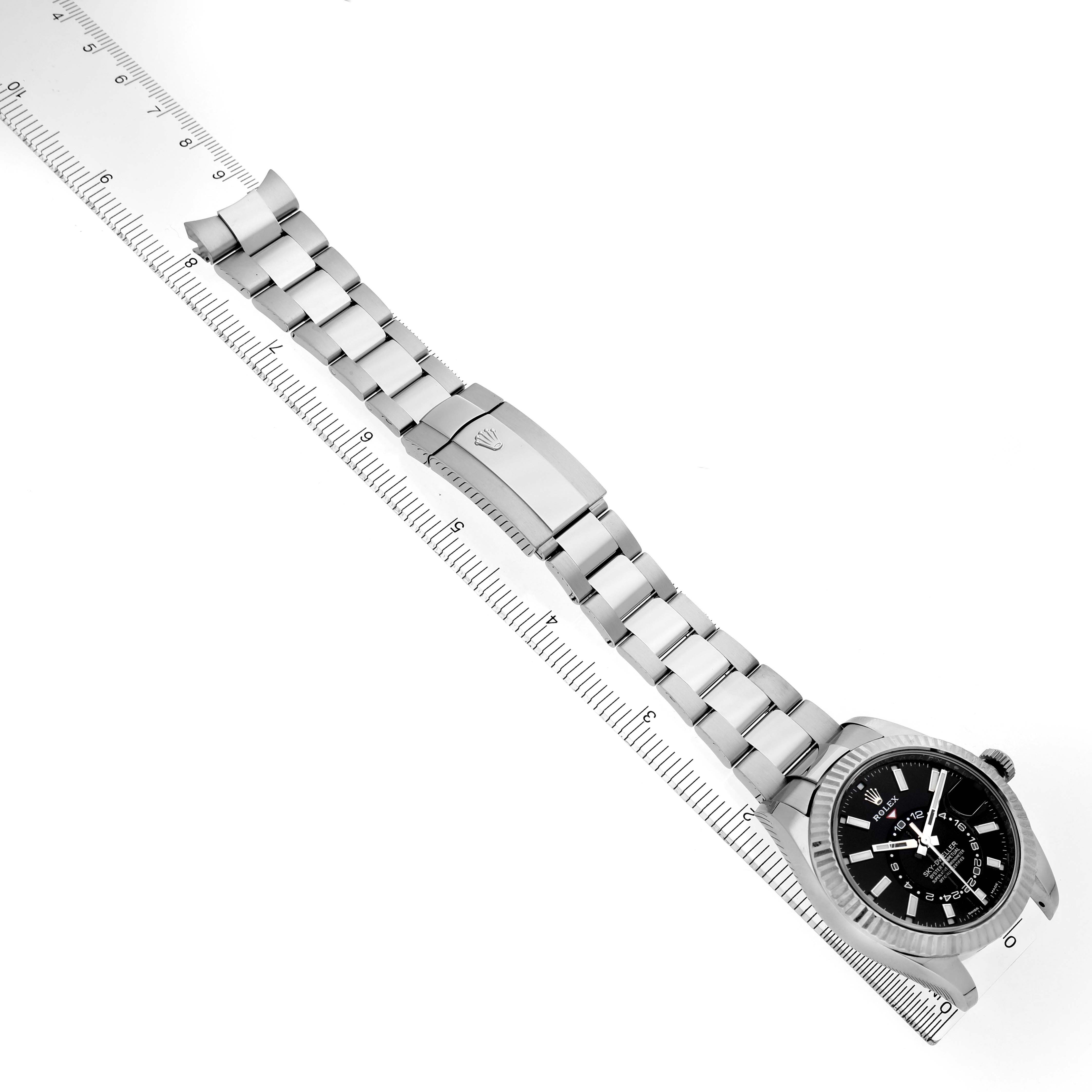 The Rolex Sky-Dweller 326934 Men's Stainless Steel Black Dial watch is shown at a slight angle with a focus on the bracelet, clasp, and face, alongside a ruler for scale.