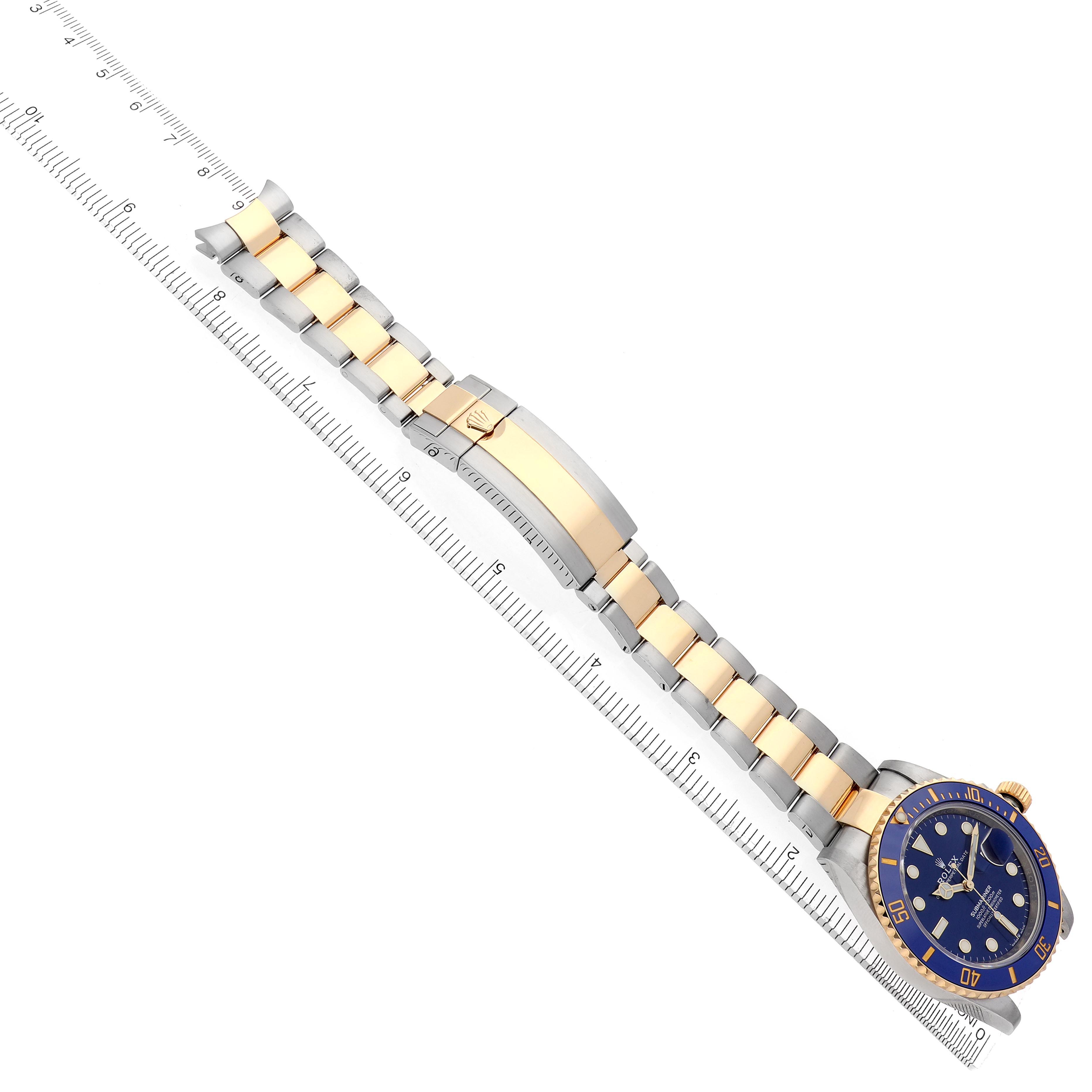 The Rolex Submariner 126613 Men
s Steel and Gold (two tone) Blue Dial 126613 Men
s Steel and Gold (two tone) Blue Dial watch is viewed from above, showing the bracelet, clasp, and face alongside a ruler.