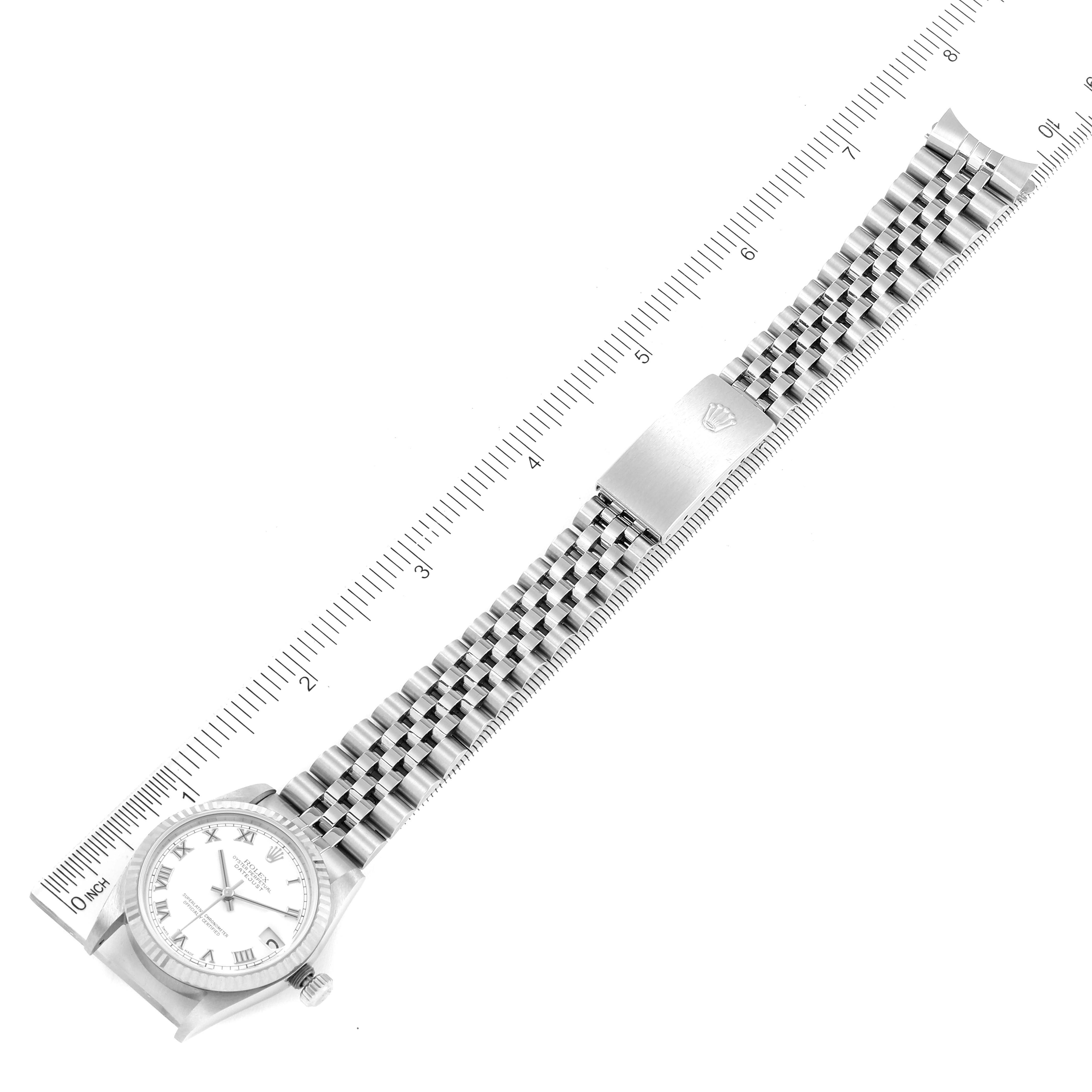 The image shows a Rolex Mid-Size 78274 Women
s Stainless Steel White Dial 78274 Women
s Stainless Steel White Dial watch from an overhead angle, highlighting its face, band, and clasp next to a ruled measurement guide.