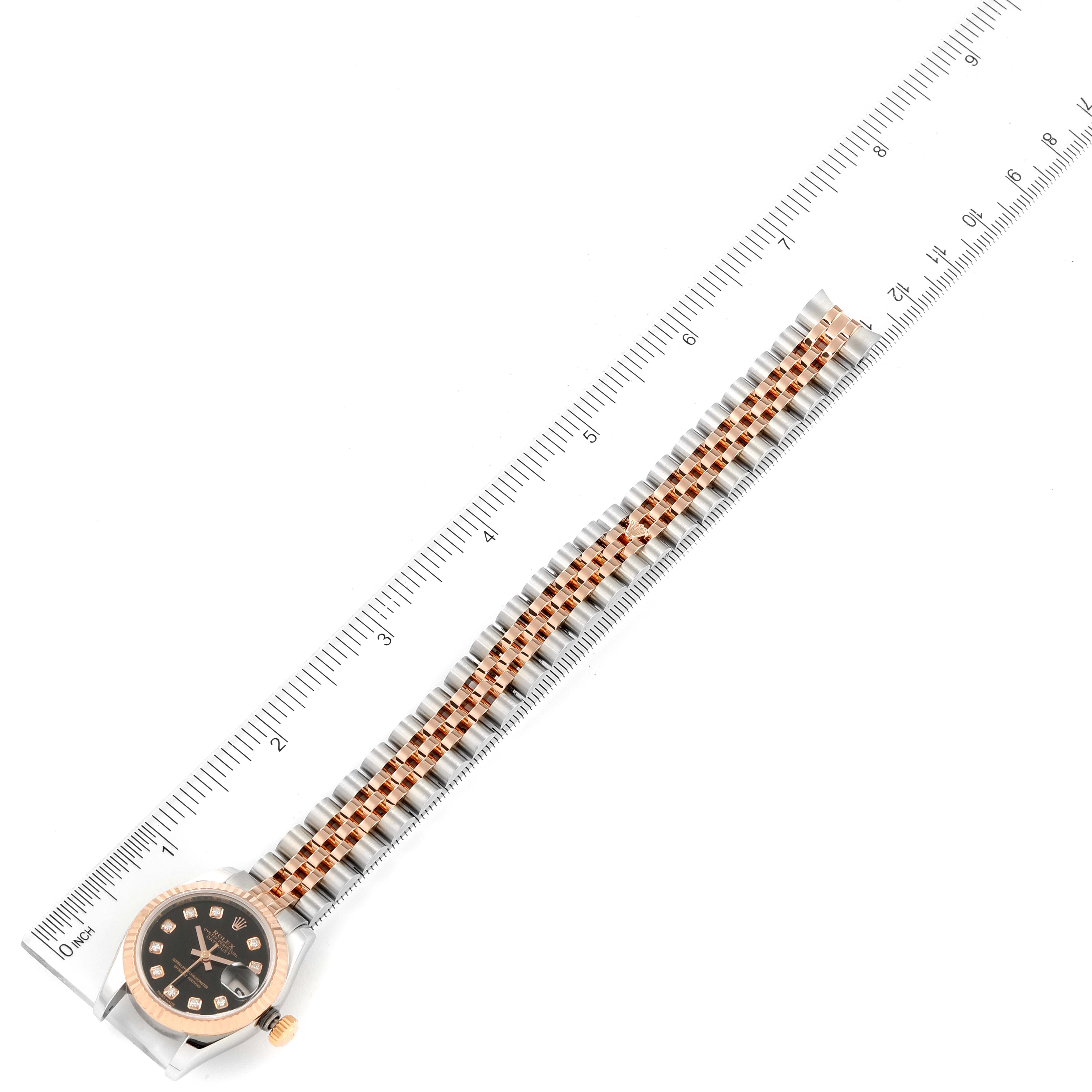 This image shows a top view of a Rolex Datejust 179171 Women
s Steel and Gold (two tone) Black Dial 179171 Women
s Steel and Gold (two tone) Black Dial watch, displaying its face, bezel, and bracelet alongside a ruler measuring its length.