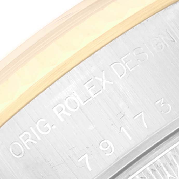 This image shows a close-up of the edge of a Rolex Datejust 79173 Women's Steel and Gold (two tone) White Dial 79173 Women's Steel and Gold (two tone) White Dial watch case with visible engravings.