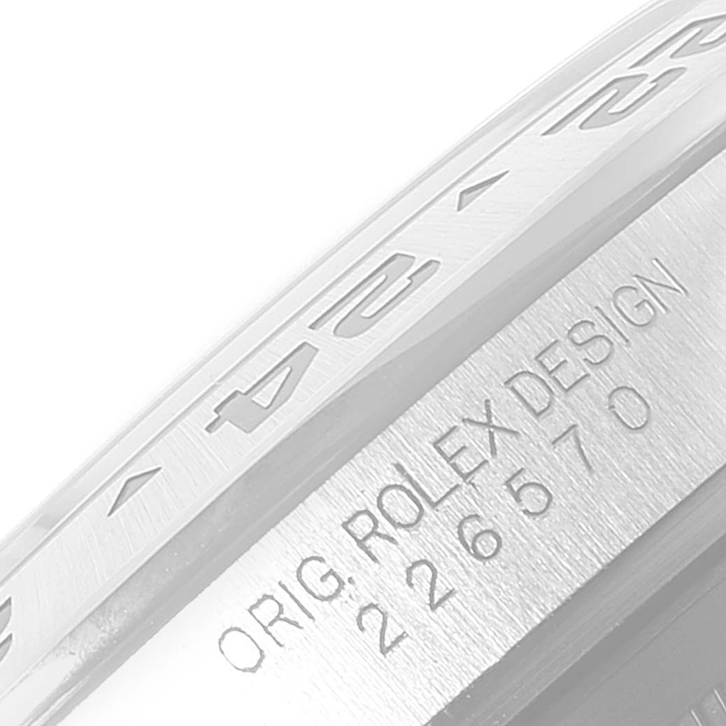 This image shows a close-up of the side of a Rolex Explorer 226570 Men's Stainless Steel Black Dial 226570 Men's Stainless Steel Black Dial's bezel, featuring its engraved numbers and "ORIG. ROLEX DESIGN" text with model number.