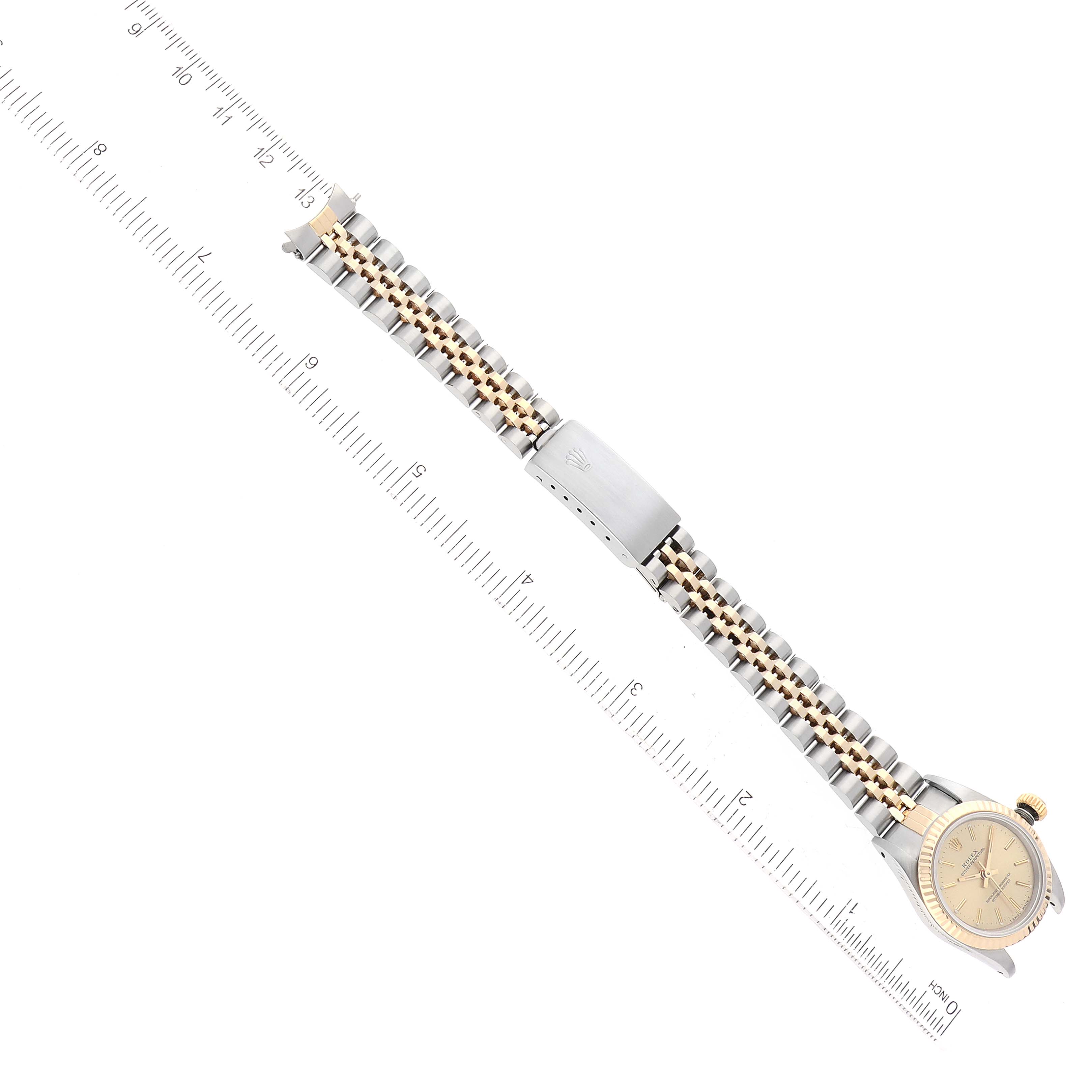 The Rolex Oyster Perpetual 67193 Women's Steel and Gold (two tone) Champagne Dial 67193 Women's Steel and Gold (two tone) Champagne Dial watch is shown from an overhead angle, displaying the dial, bracelet, and clasp with a ruler for scale.