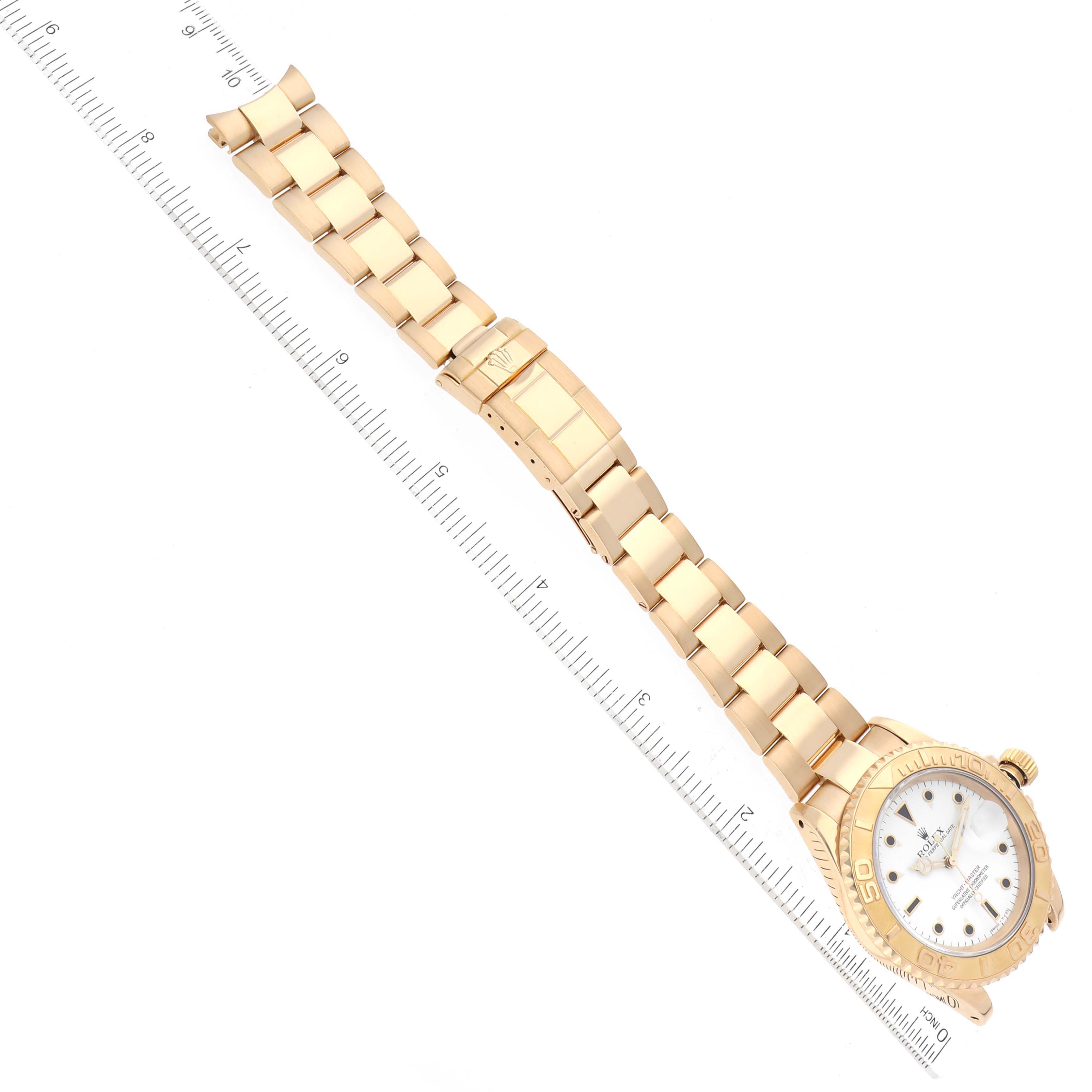 This image shows a top-down view of a Rolex Yacht-Master 16628 Men's Yellow Gold White Dial 16628 Men's Yellow Gold White Dial watch with a gold bracelet and a ruler for scale.