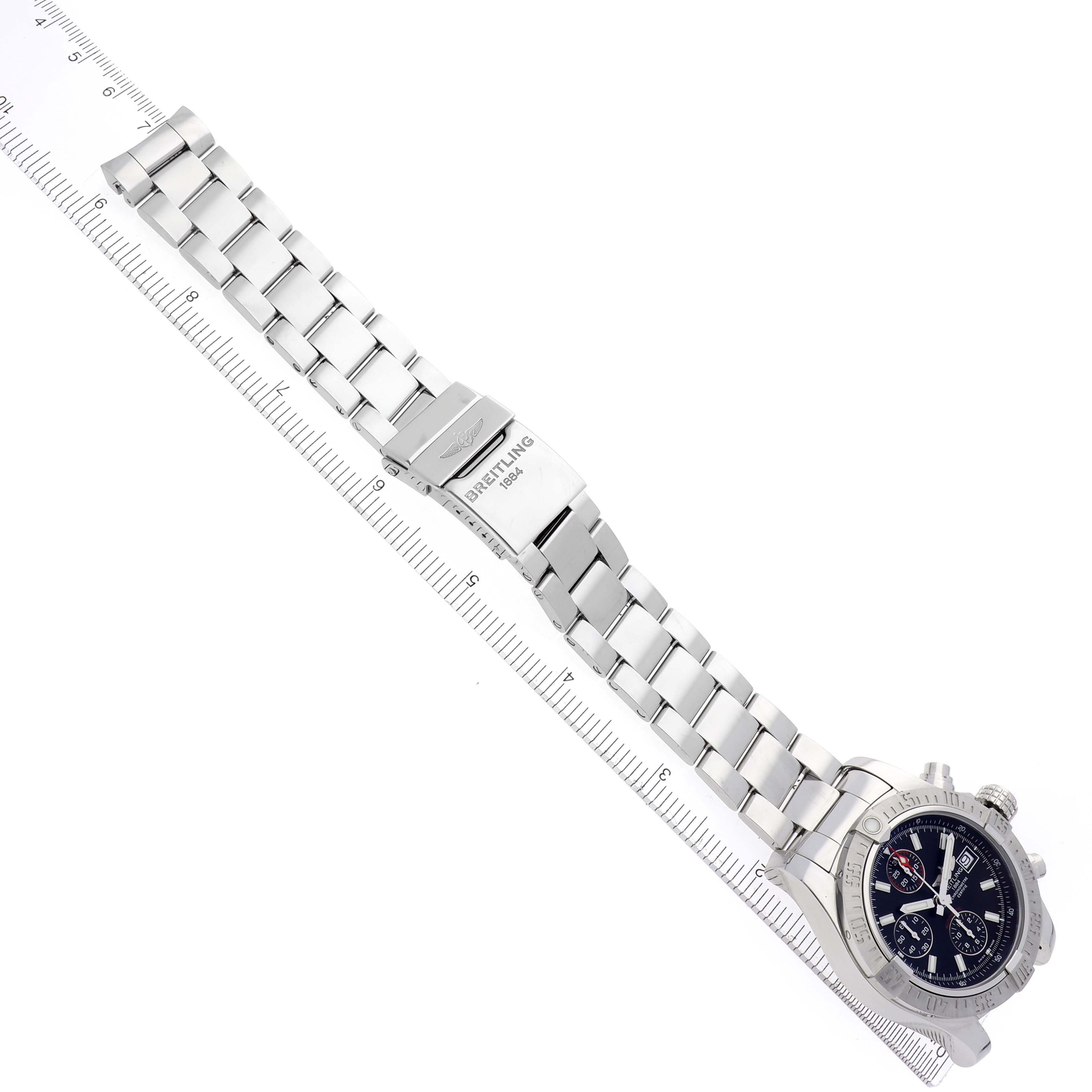 The Breitling Avenger A13381 Men
s Stainless Steel Black Dial A13381 Men
s Stainless Steel Black Dial watch is displayed at a diagonal angle, showcasing the bracelet, clasp, and face alongside a ruler.