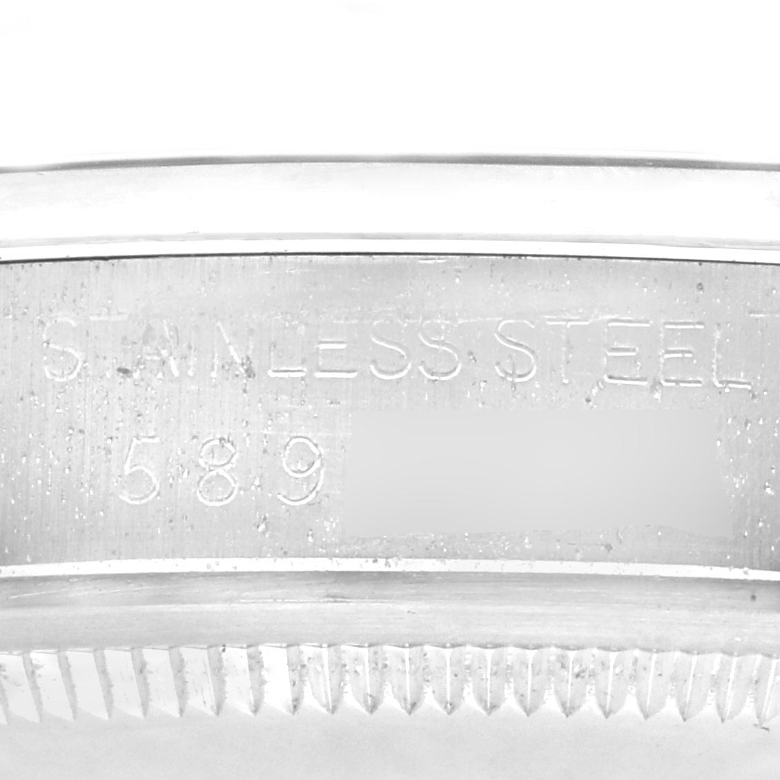 The image shows a close-up of the inner bezel and edge of a Rolex Date watch, highlighting the stainless steel text and part number.
