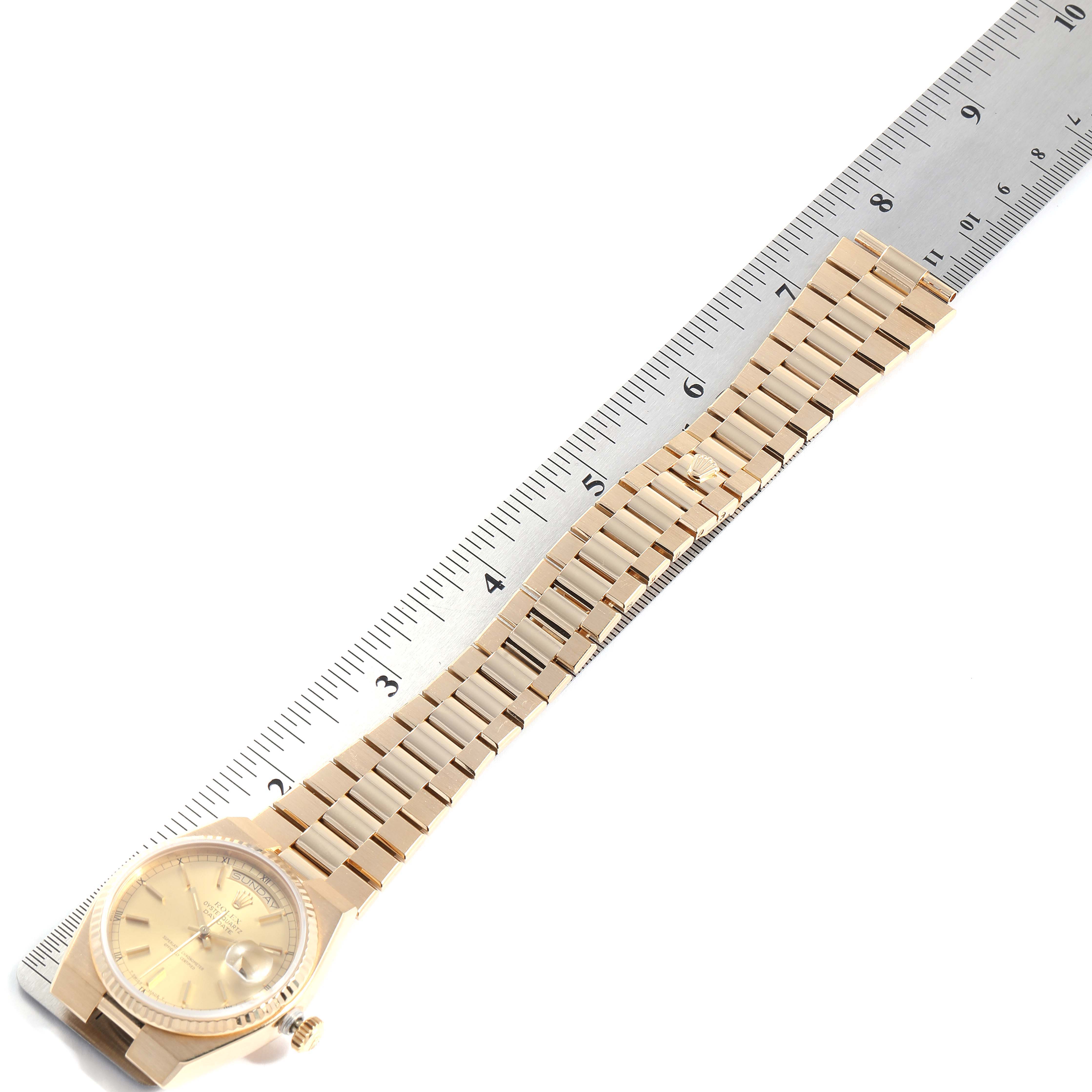 This image shows a President model Rolex watch laying flat next to a 12-inch ruler, displaying its band and face.