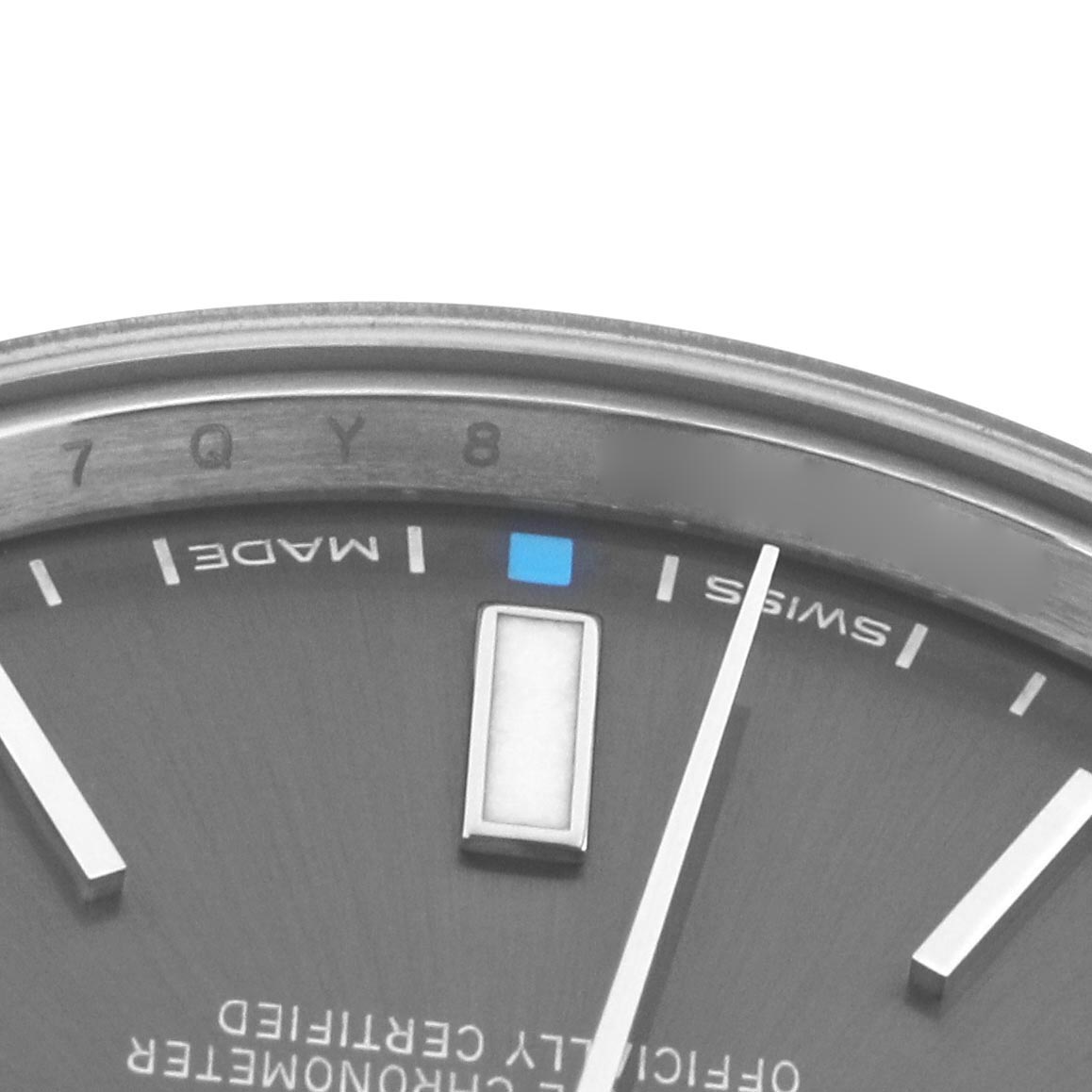 The image shows a close-up of the Rolex Oyster Perpetual 114300 Men
s Stainless Steel Grey Dial 114300 Men
s Stainless Steel Grey Dial
s dial, focusing on the hour markers, hands, and partial text.