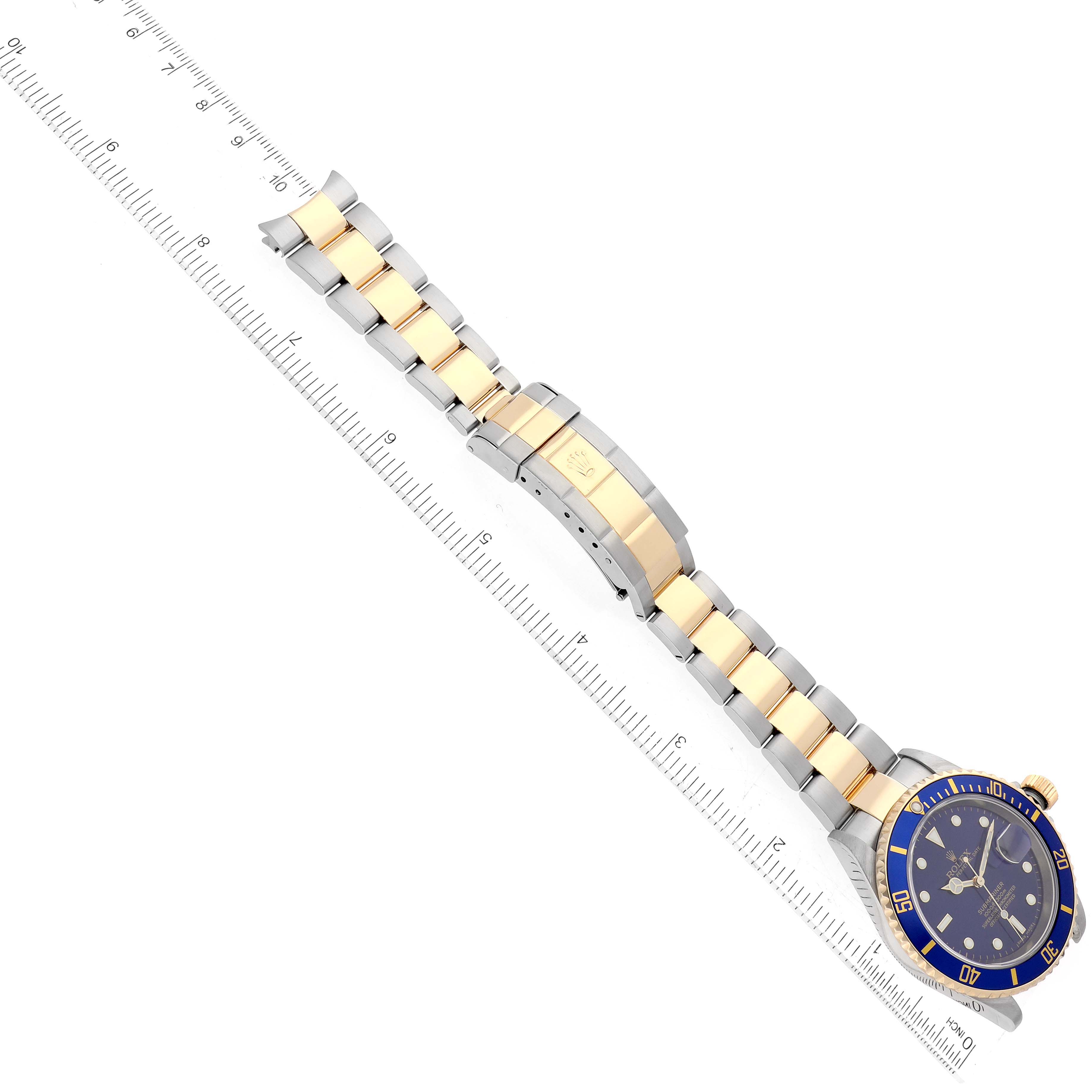 The image shows a top-down view of a Rolex Submariner 16613 Men's Steel and Gold (two tone) Blue Dial 16613 Men's Steel and Gold (two tone) Blue Dial watch with a two-tone bracelet next to a ruler.