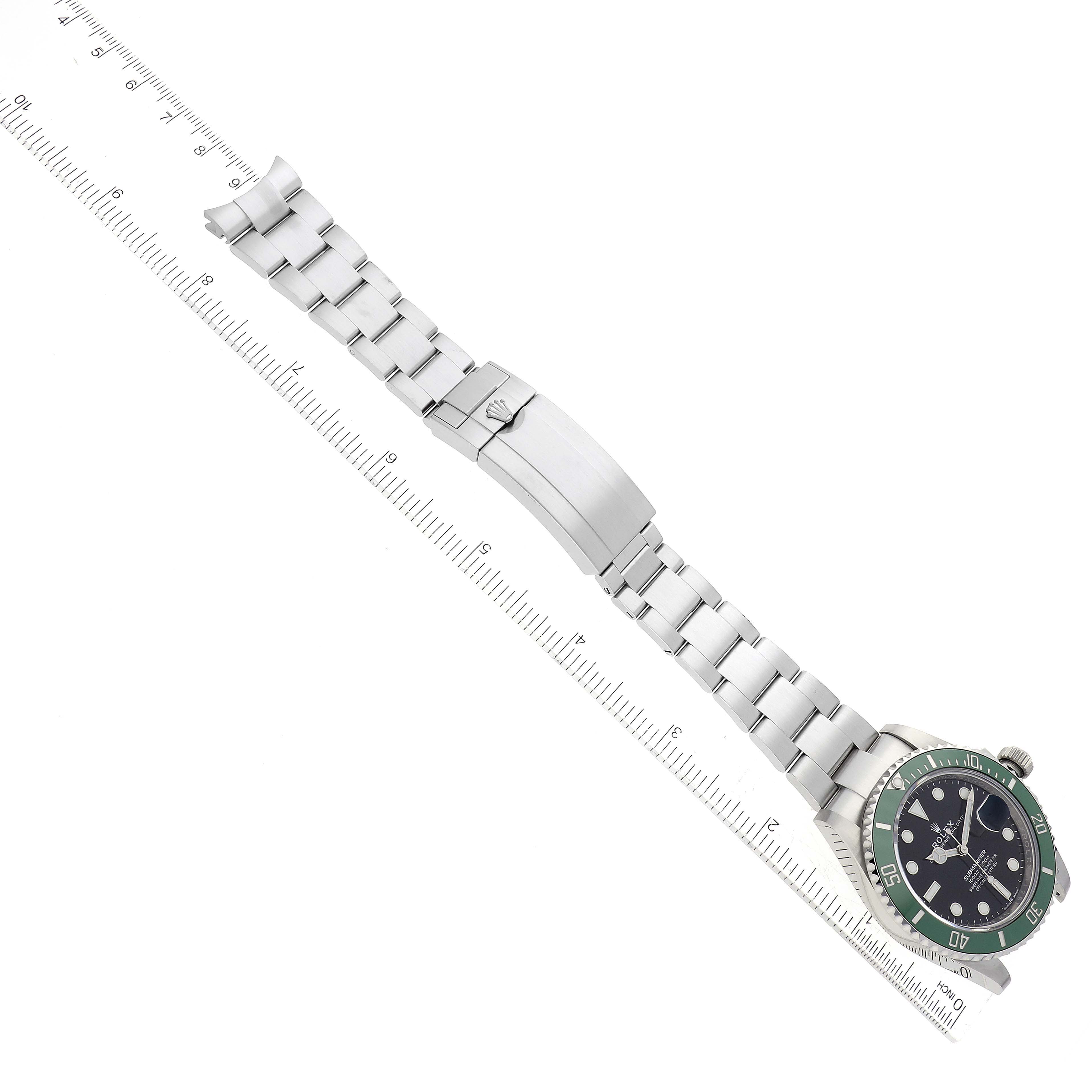 The image shows a top-down view of a Rolex Submariner 126610LV Men's Stainless Steel Black Dial 126610LV Men's Stainless Steel Black Dial watch with a green bezel and metal bracelet next to a ruler.