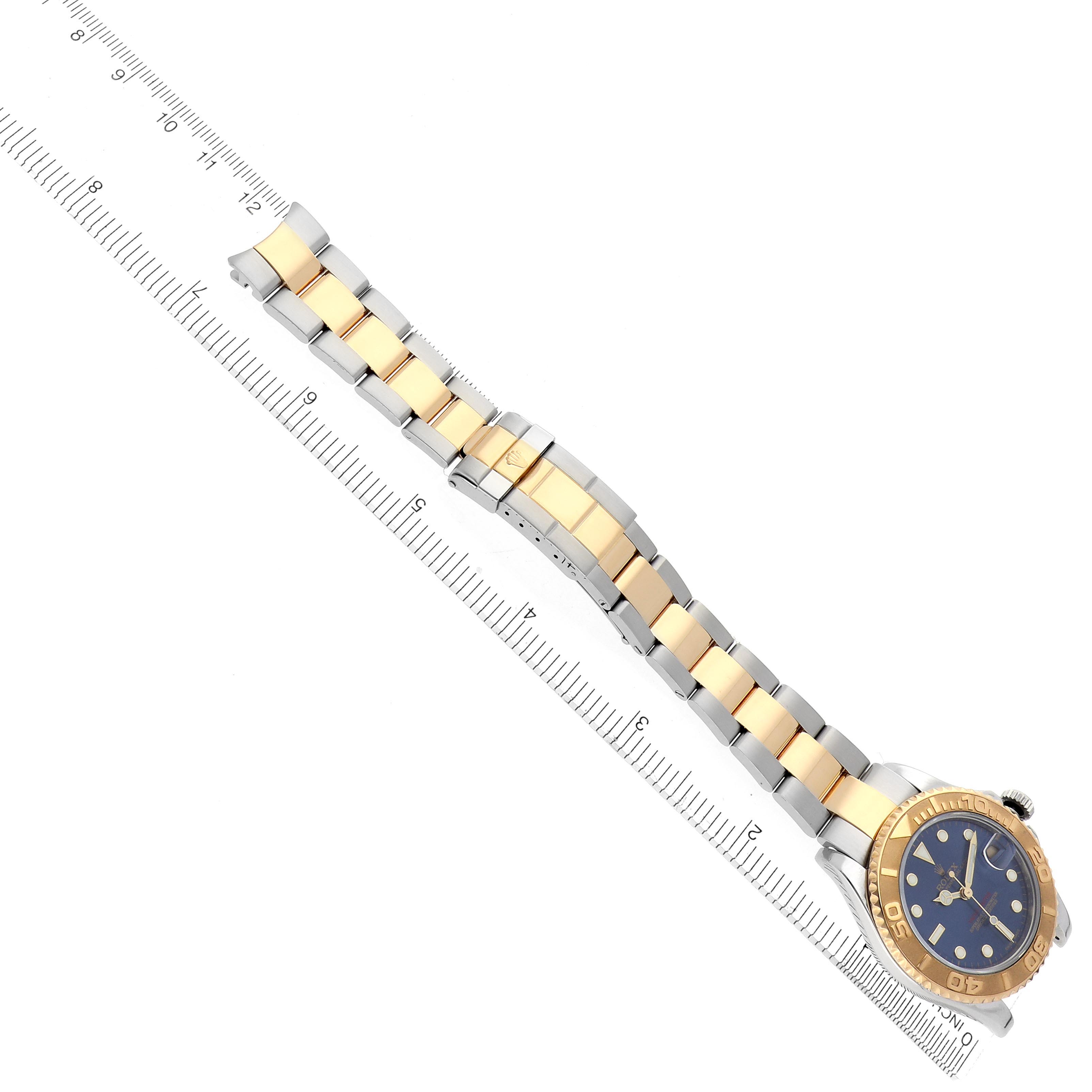 The image shows a Rolex Yacht-Master 168623 Men
s Steel and Gold (two tone) Blue Dial 168623 Men
s Steel and Gold (two tone) Blue Dial watch laid flat, displaying the dial, bezel, and bracelet alongside a ruler for scale.