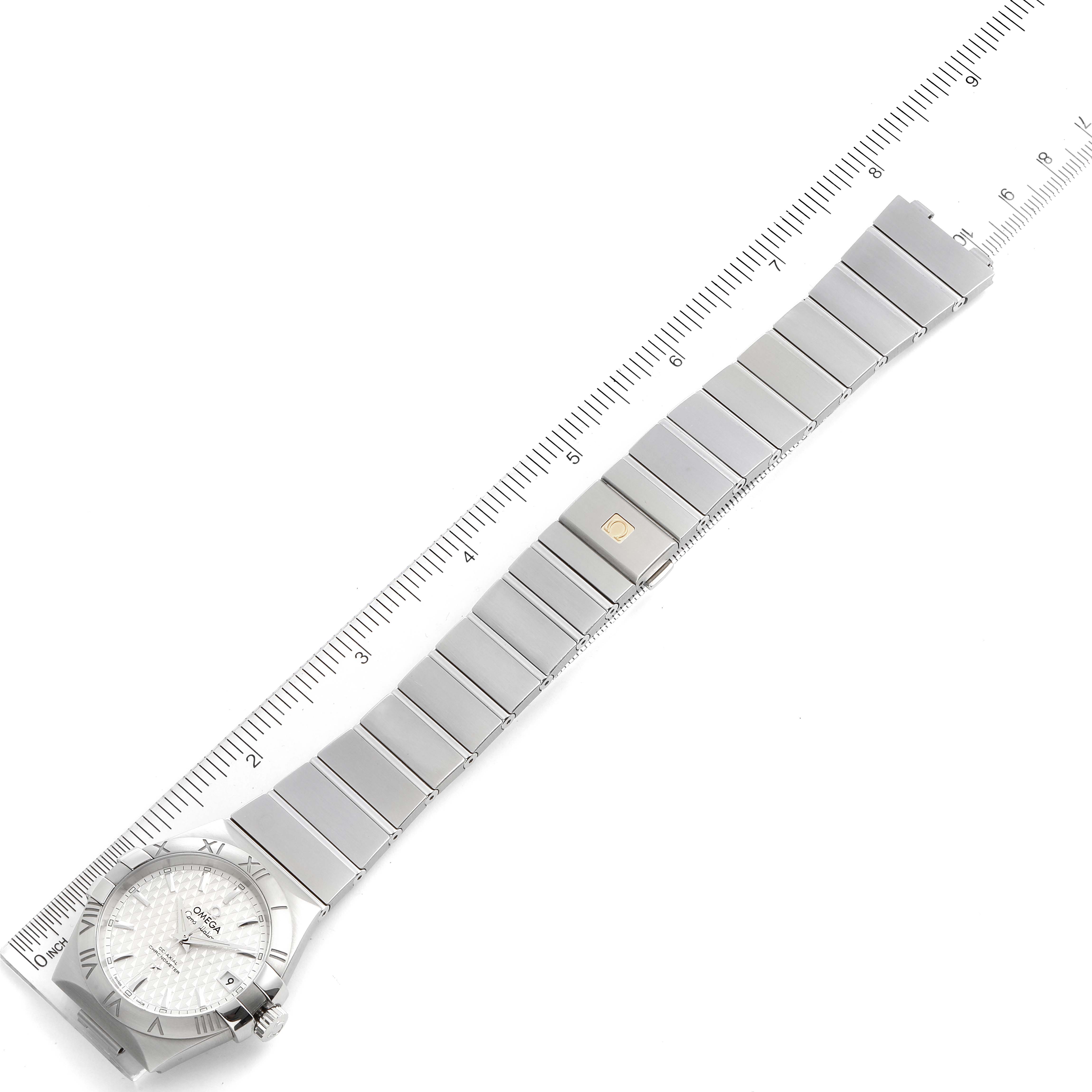 The image shows an overhead view of an Omega Constellation 123.10.35.20.02.002  Men
s Stainless Steel Silver Dial 123.10.35.20.02.002  Men
s Stainless Steel Silver Dial watch with a ruler alongside, revealing its face and full bracelet.