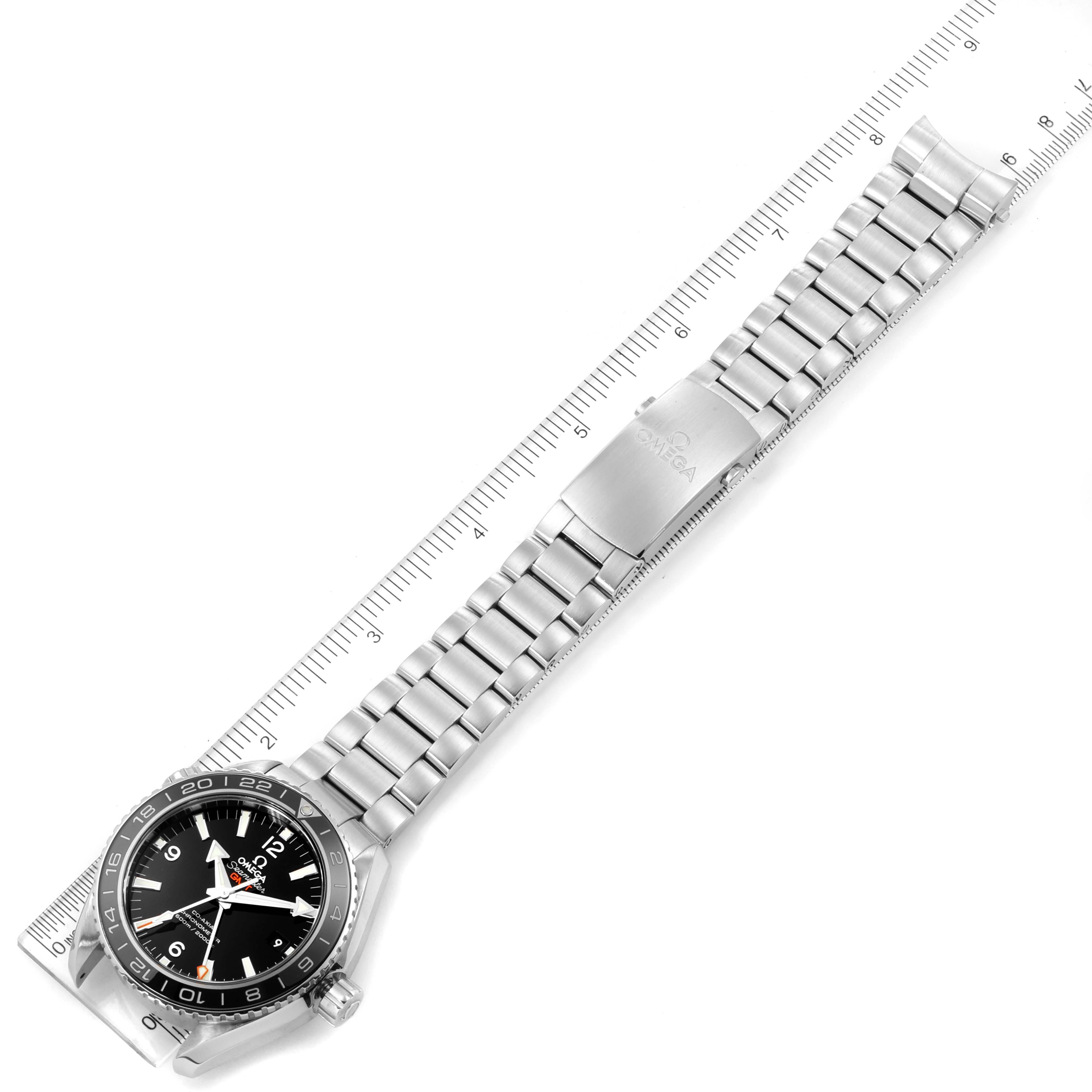 The image shows an overhead view of the Omega Planet Ocean 232.30.44.22.01.001 Men
s Stainless Steel Black Dial 232.30.44.22.01.001 Men
s Stainless Steel Black Dial watch, including its face, bezel, and metal bracelet lying next to a ruler.