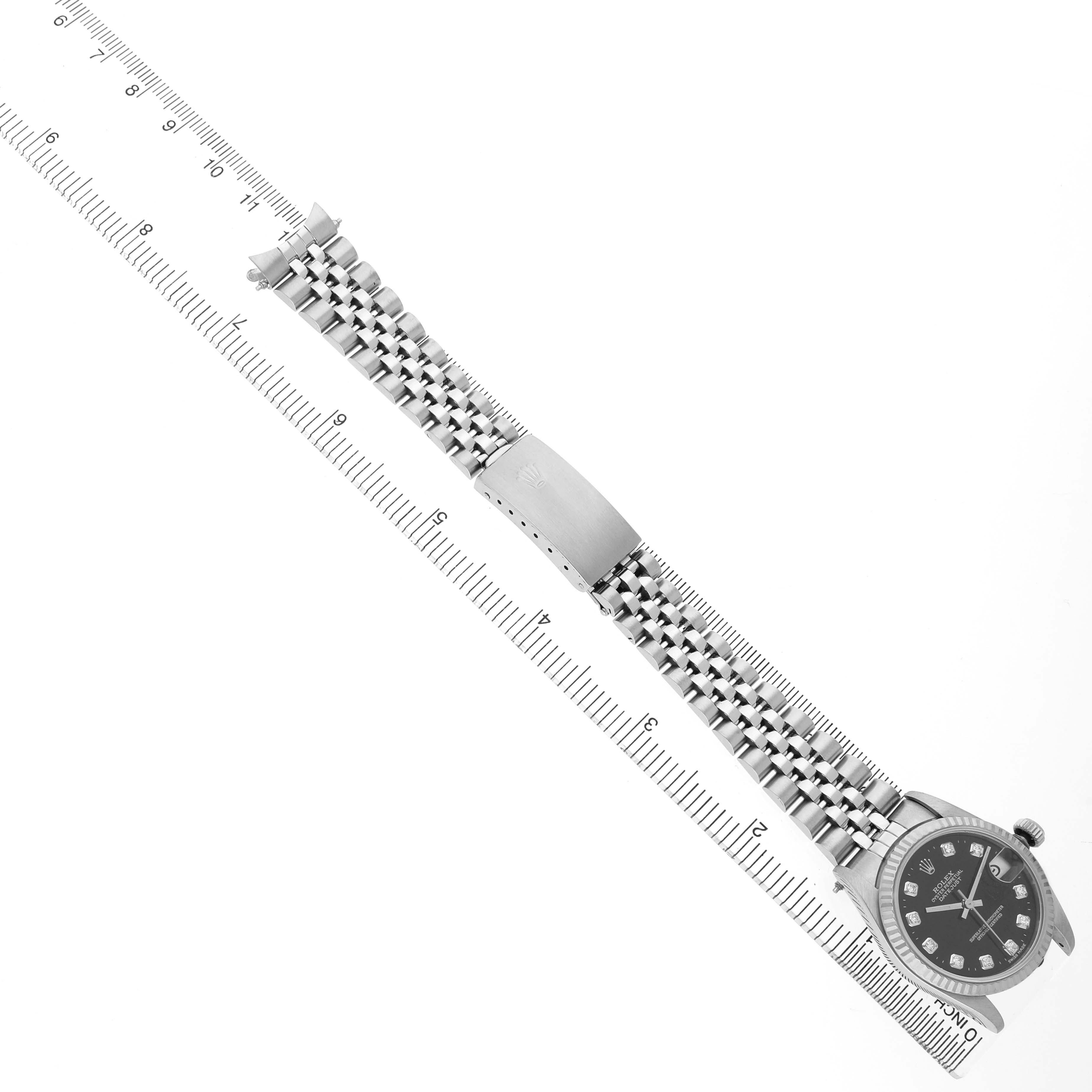 The Rolex Mid-Size 68274 Women's Stainless Steel Black Dial watch is shown from a top-down angle, displaying the face, bracelet, and clasp alongside a measuring ruler.