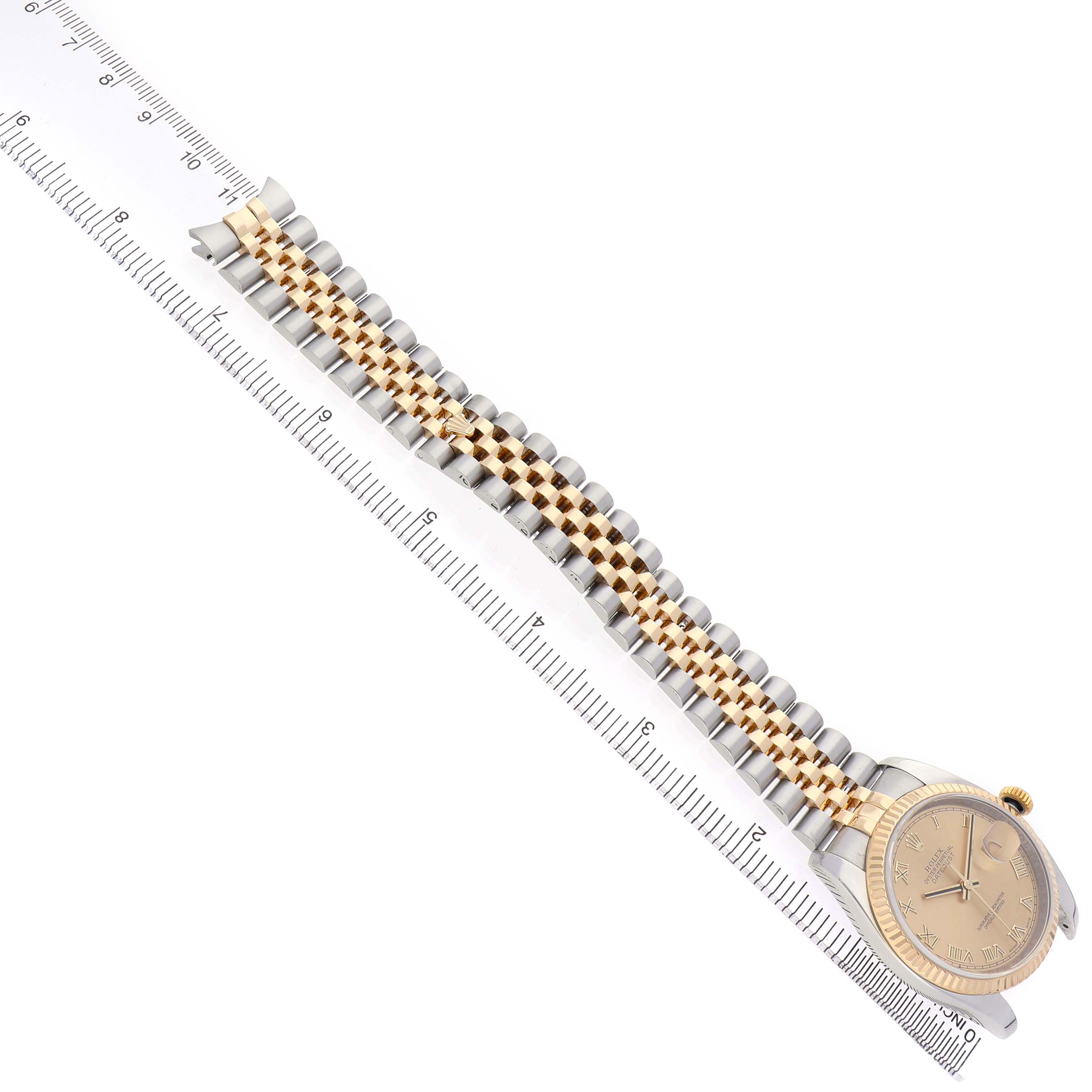 The Rolex Datejust 116233 Men's Stainless Steel Champagne Dial is shown from an overhead angle, highlighting the bracelet and face alongside a ruler for scale.