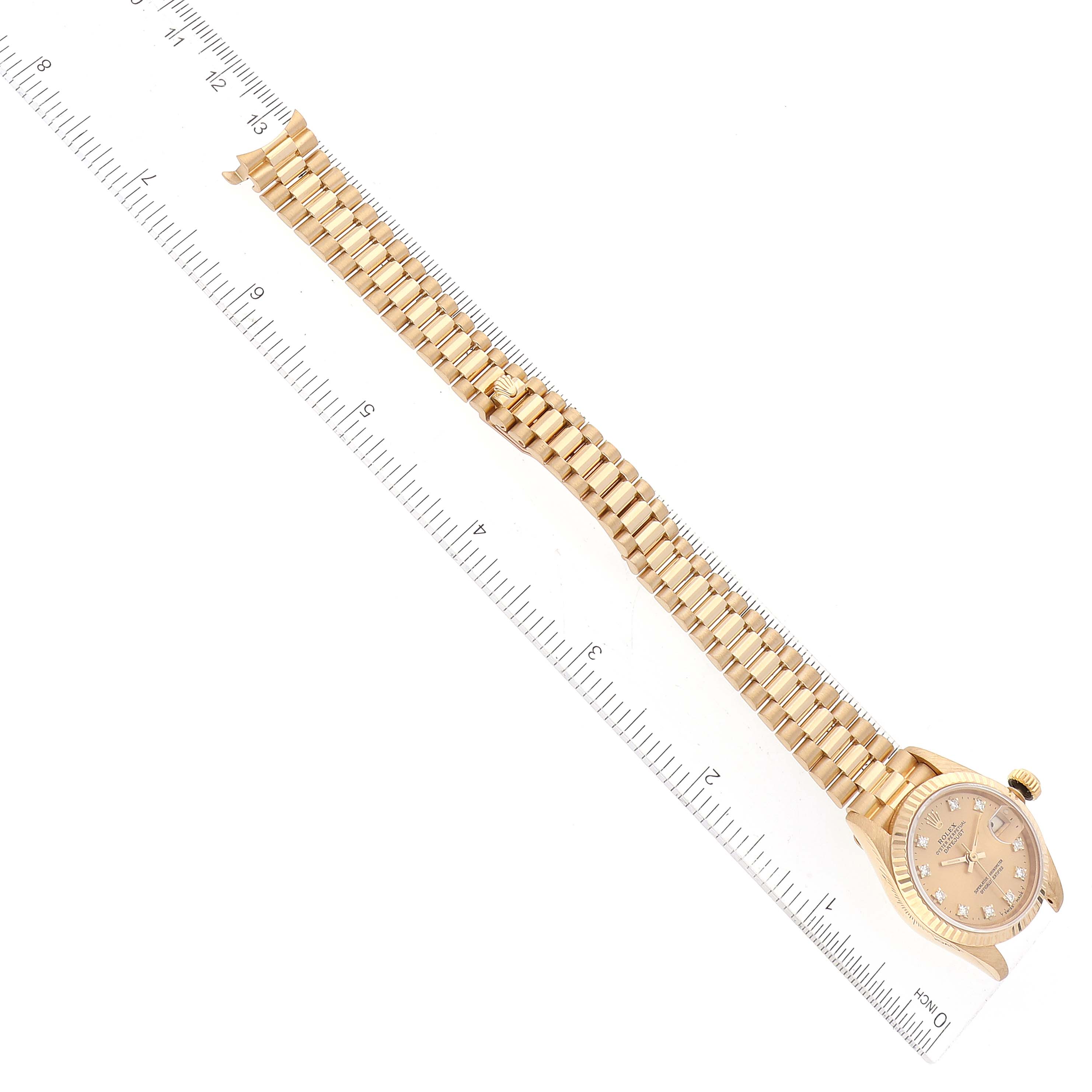 This image shows a Rolex President 69178 Women
s Yellow Gold Champagne Dial 69178 Women
s Yellow Gold Champagne Dial model watch from a top-down angle, including the watch face and full-length bracelet, placed alongside a ruler for scale.