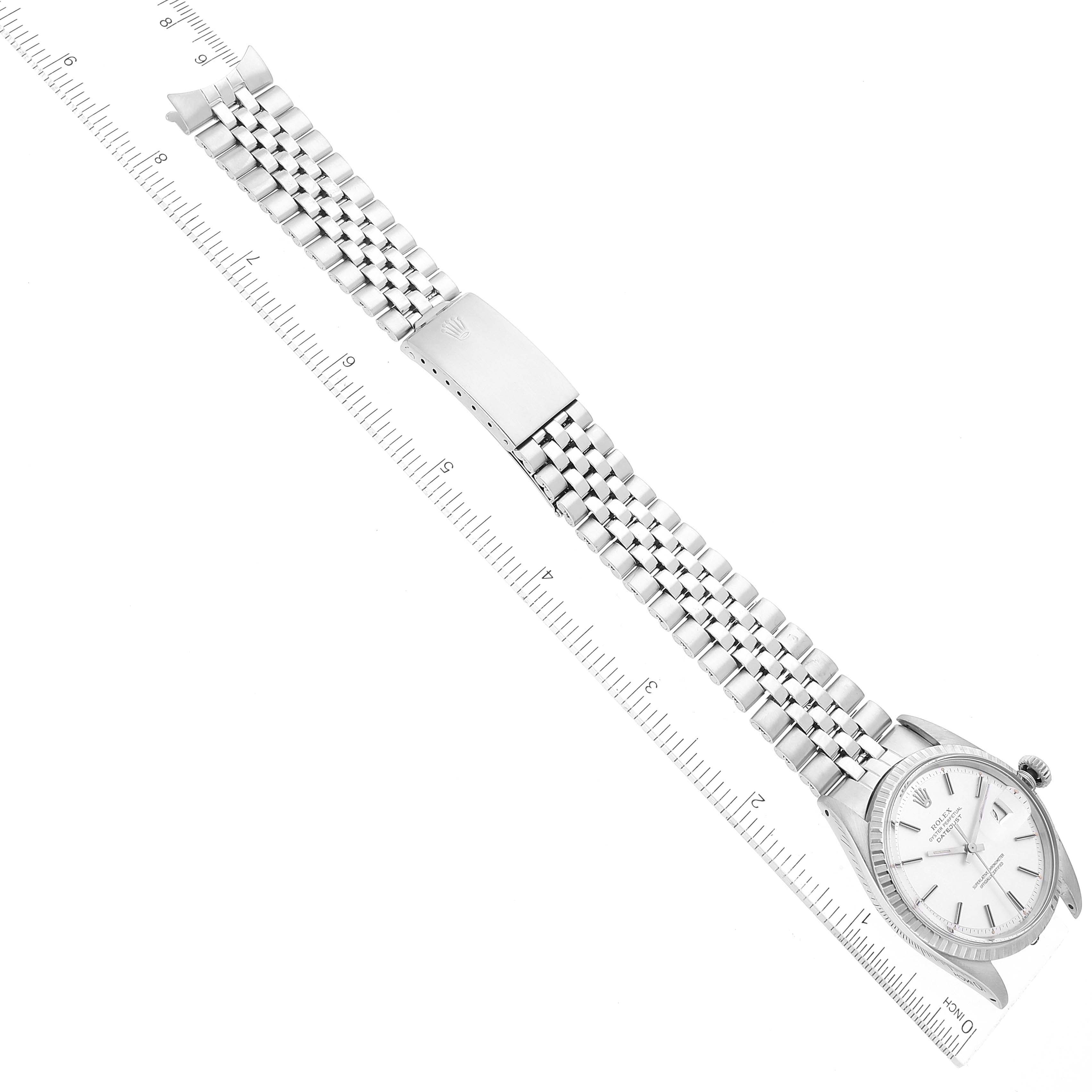 The Rolex Datejust 1603 Men's Stainless Steel Silver Dial 1603 Men's Stainless Steel Silver Dial watch is shown from an overhead angle, featuring the dial, bezel, bracelet, and clasp alongside a measuring ruler.