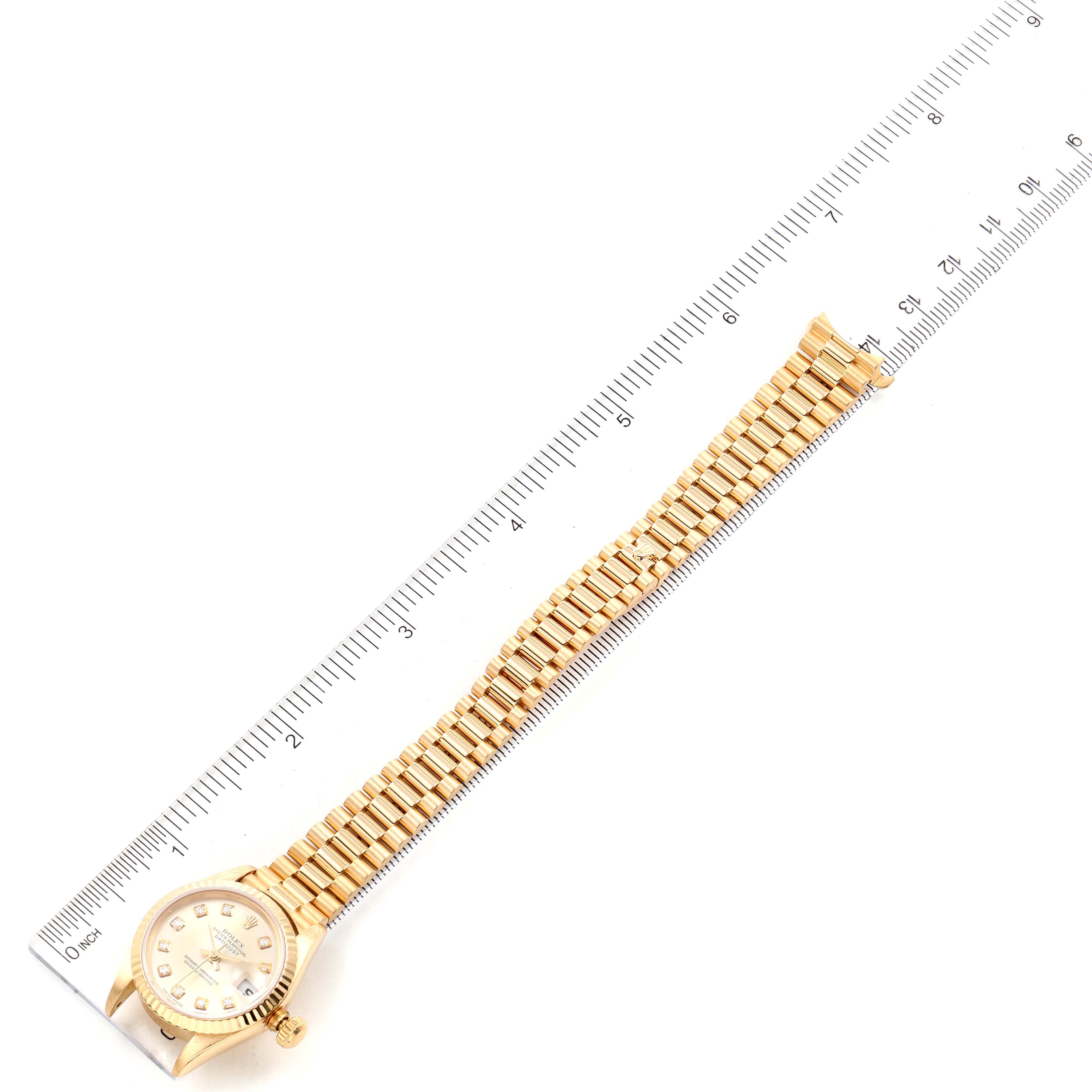 The image shows a Rolex President 79178 Women
s Yellow Gold Champagne Dial 79178 Women
s Yellow Gold Champagne Dial model watch laying flat with its face, bezel, band, and clasp visible next to a ruler.