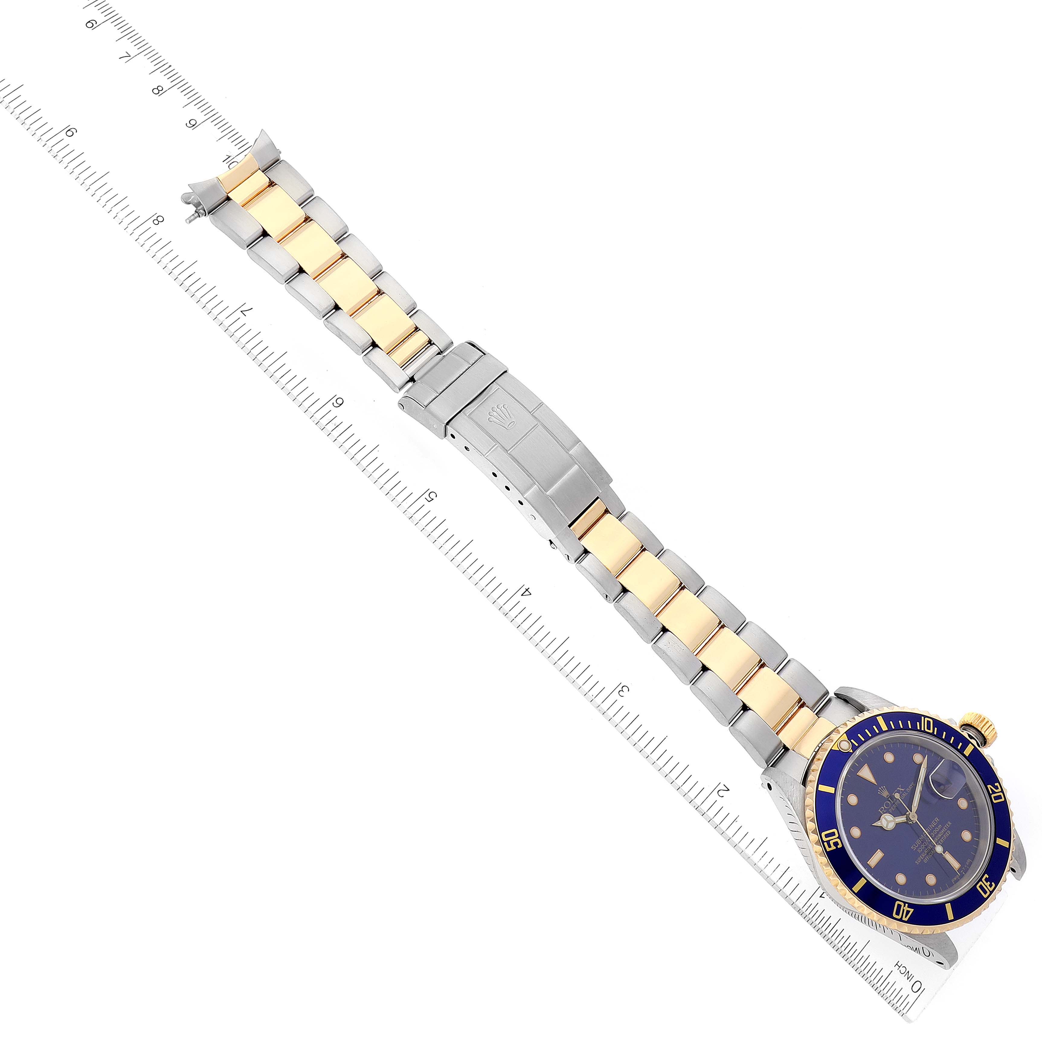 This top-down view of a Rolex Submariner 16613 Men's Steel and Gold (two tone) Blue Dial 16613 Men's Steel and Gold (two tone) Blue Dial shows the entire watch and bracelet, positioned over a ruler.