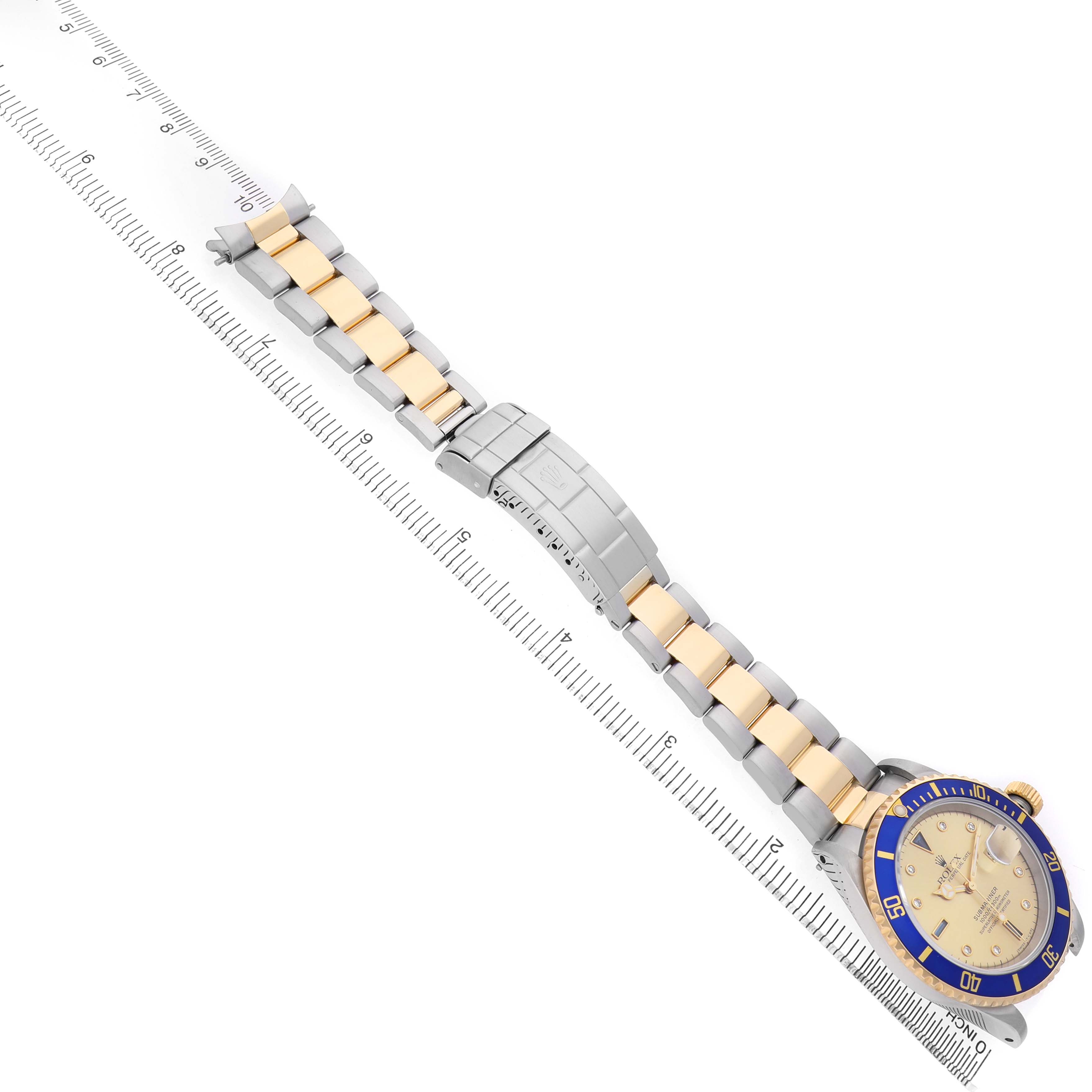 The Rolex Submariner 16613 Men's Steel and Gold (two tone) Champagne Dial watch is shown from a top view, displaying the full bracelet and face alongside a ruler for scale.