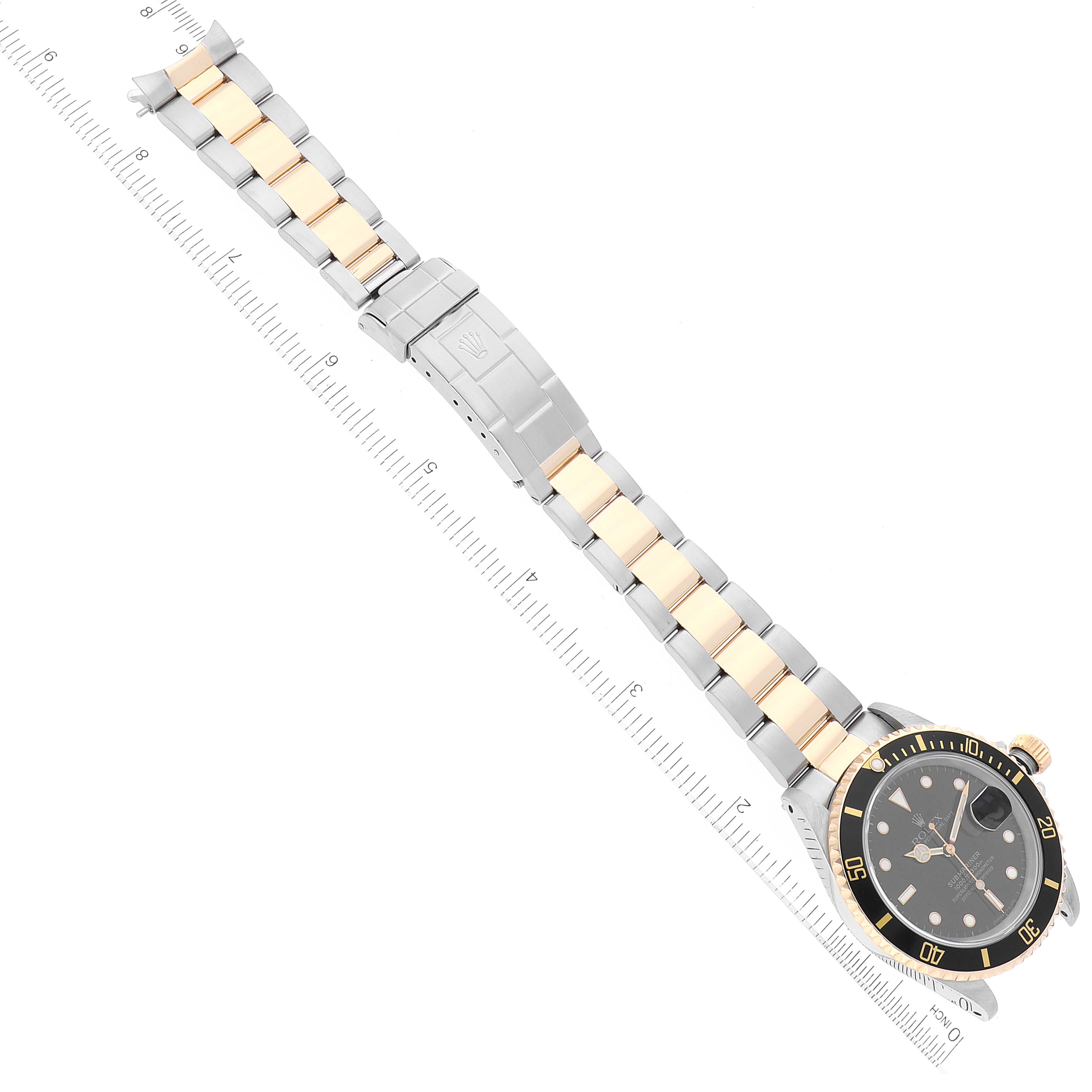 The image shows a top-down view of a Rolex Submariner 16613 Men's Steel and Gold (two tone) Black Dial 16613 Men's Steel and Gold (two tone) Black Dial, highlighting its full two-tone bracelet and face next to a ruler.