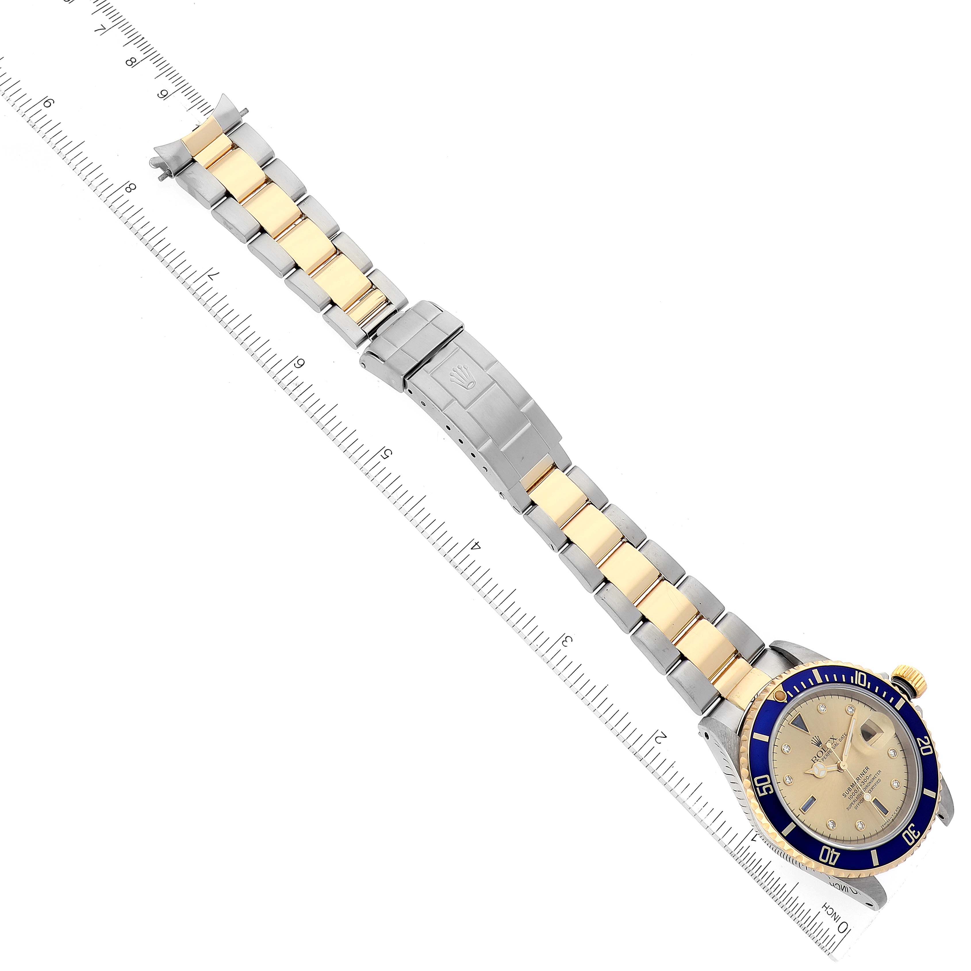 This image shows a Rolex Submariner 16613 Men's Steel and Gold (two tone) Champagne Dial 16613 Men's Steel and Gold (two tone) Champagne Dial watch lying flat with its gold and silver bracelet fully extended and a ruler next to it.
