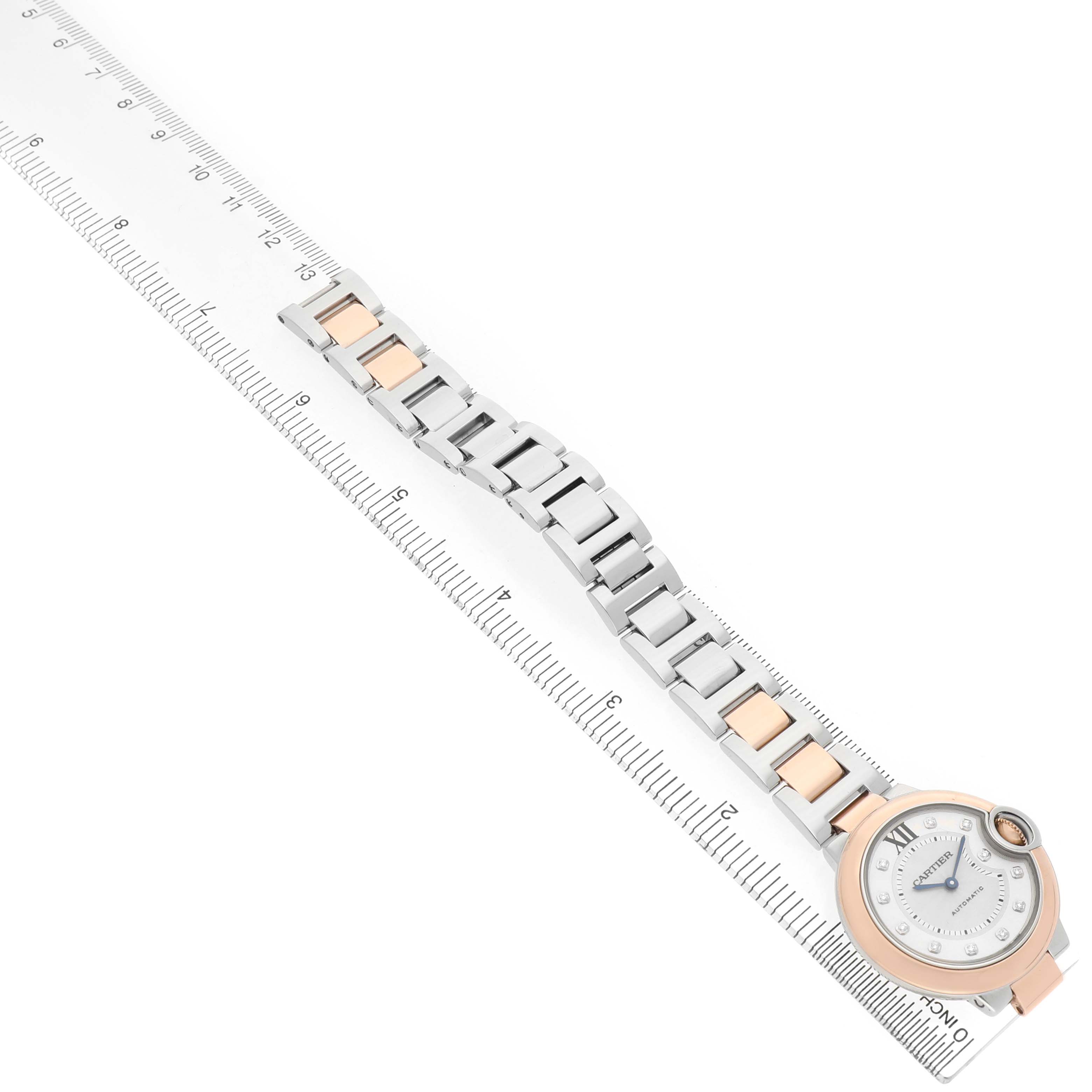 The Ballon Bleu de Cartier watch is displayed from an overhead angle, with its bracelet extended alongside a ruler.