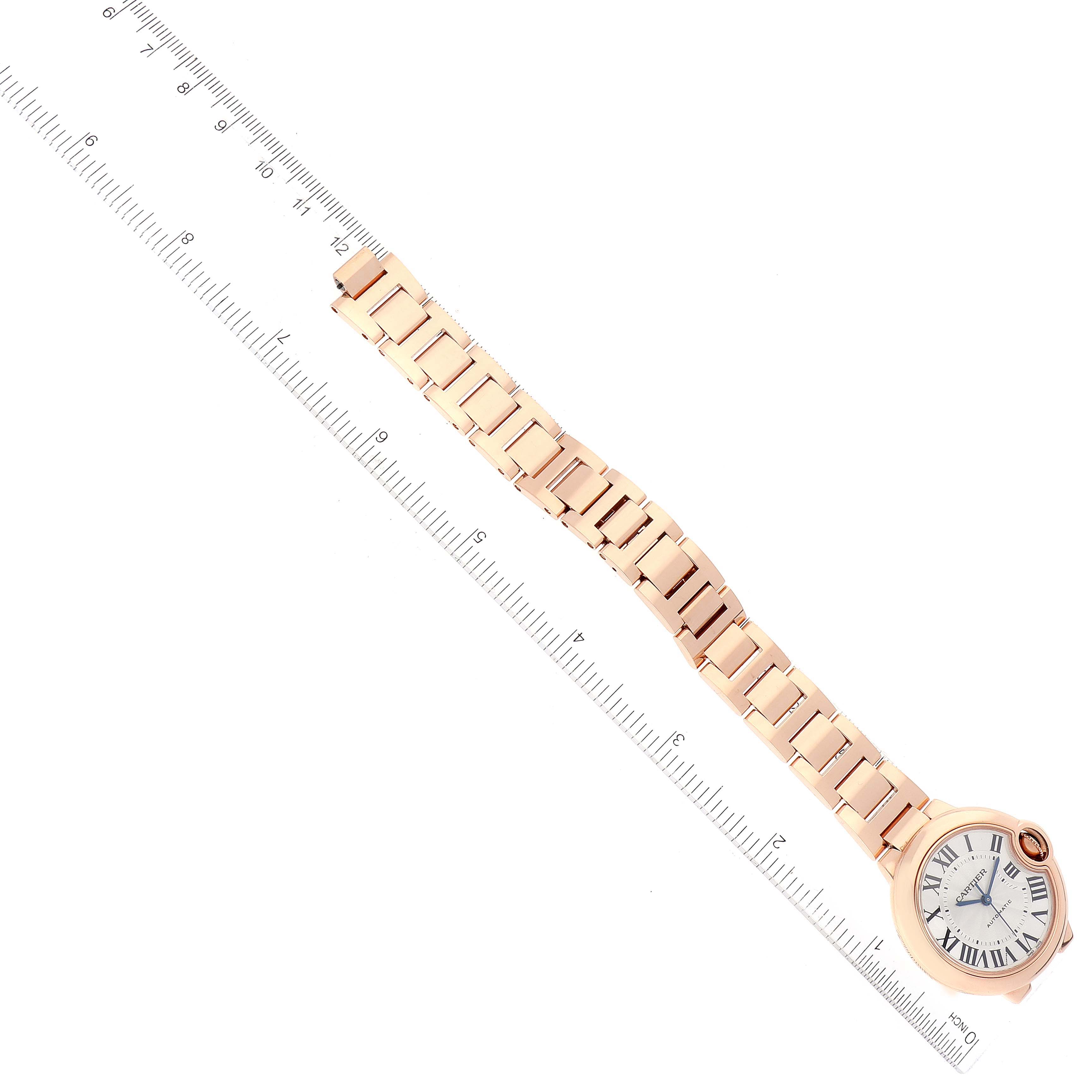 The Cartier Ballon Bleu WGBB0042 Women's Rose Gold Silver Dial WGBB0042 Women's Rose Gold Silver Dial watch is shown from a top-down angle, displaying its circular face and metal bracelet alongside a ruler for scale.