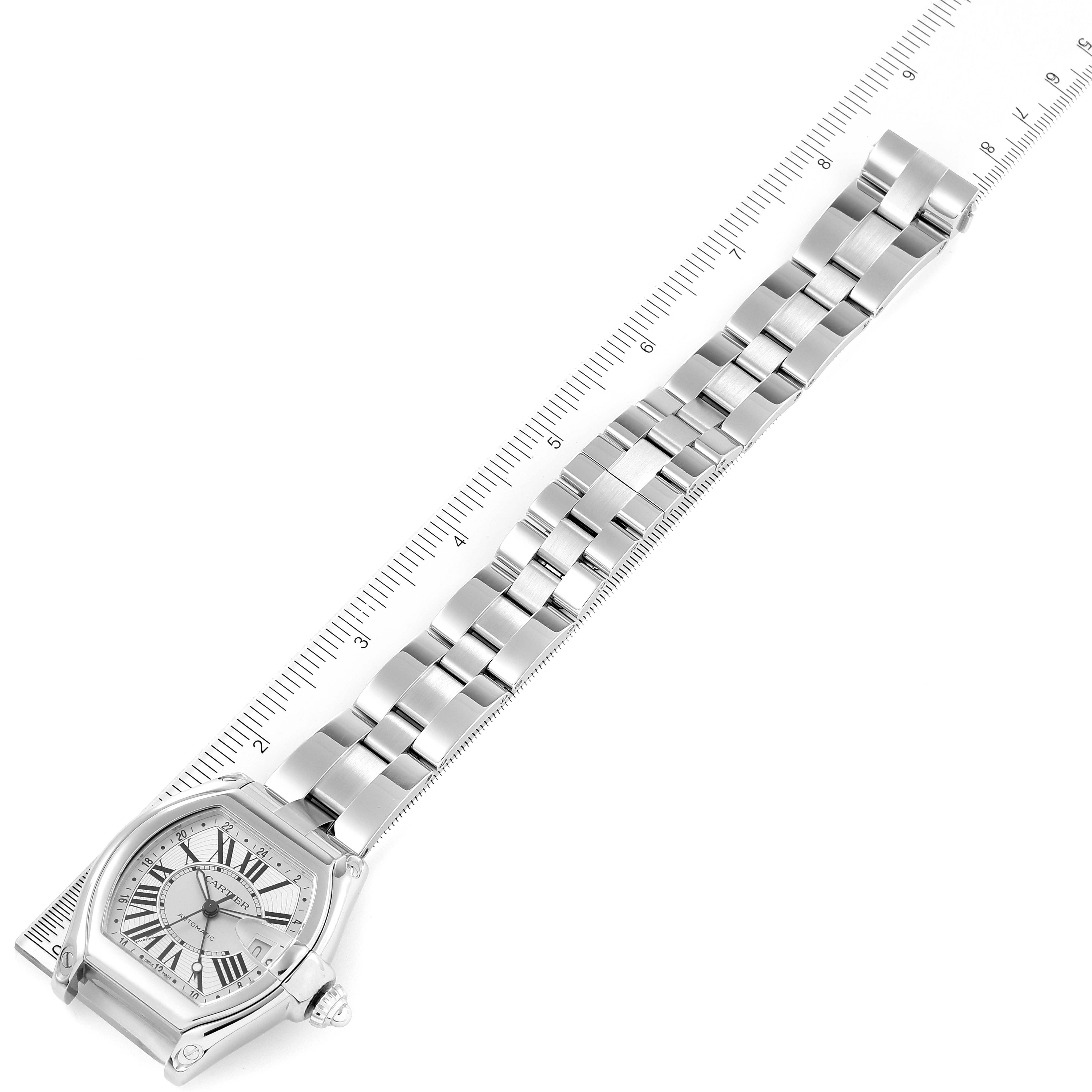 This image shows a Cartier Roadster W62032X6 Men
s Stainless Steel Silver Dial W62032X6 Men
s Stainless Steel Silver Dial watch from an overhead angle, displaying its face and metal bracelet laid out on a ruler.