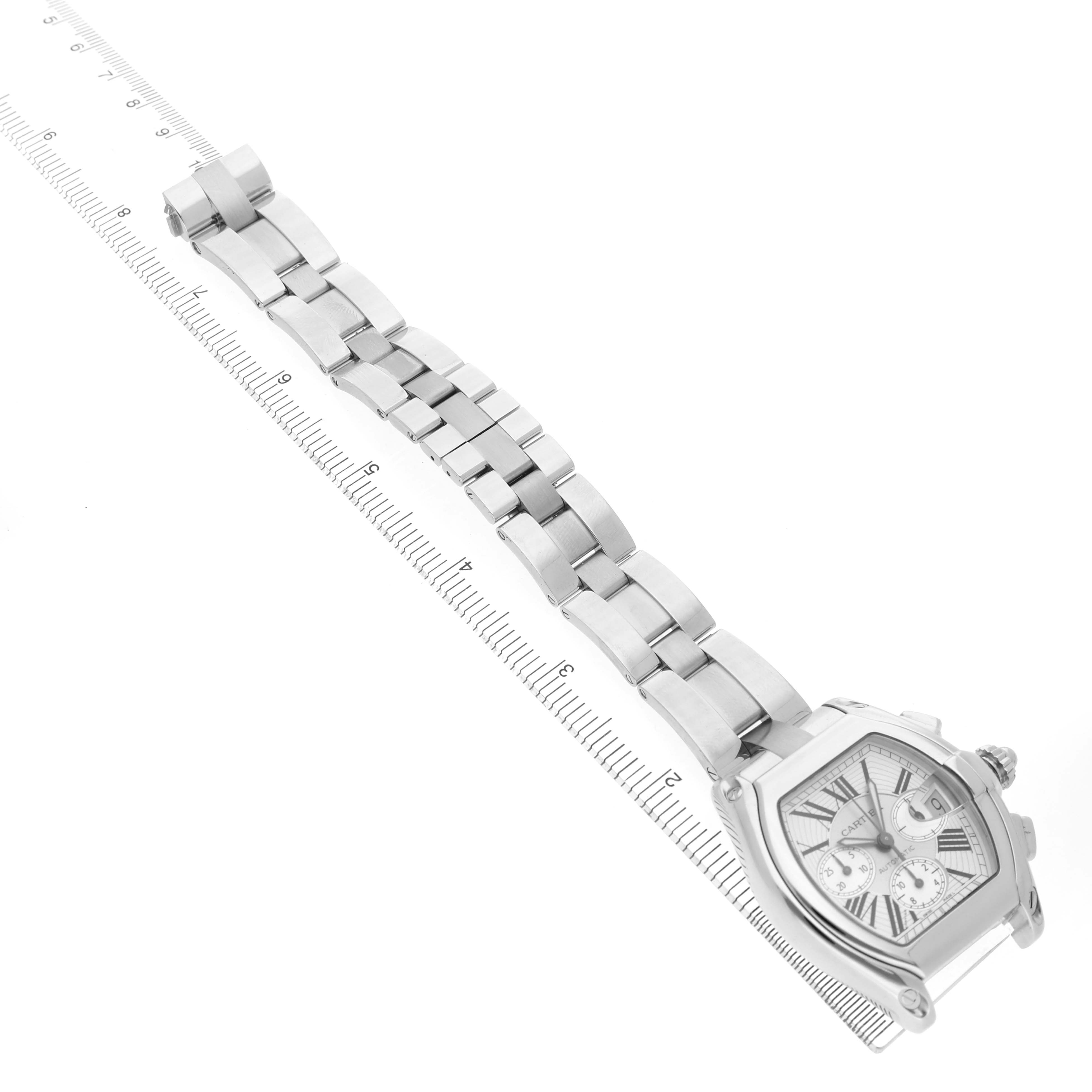 The Cartier Roadster W62019X6 Men's Stainless Steel Silver Dial watch is shown at an angle, displaying the face, case, and metal bracelet alongside a ruler.