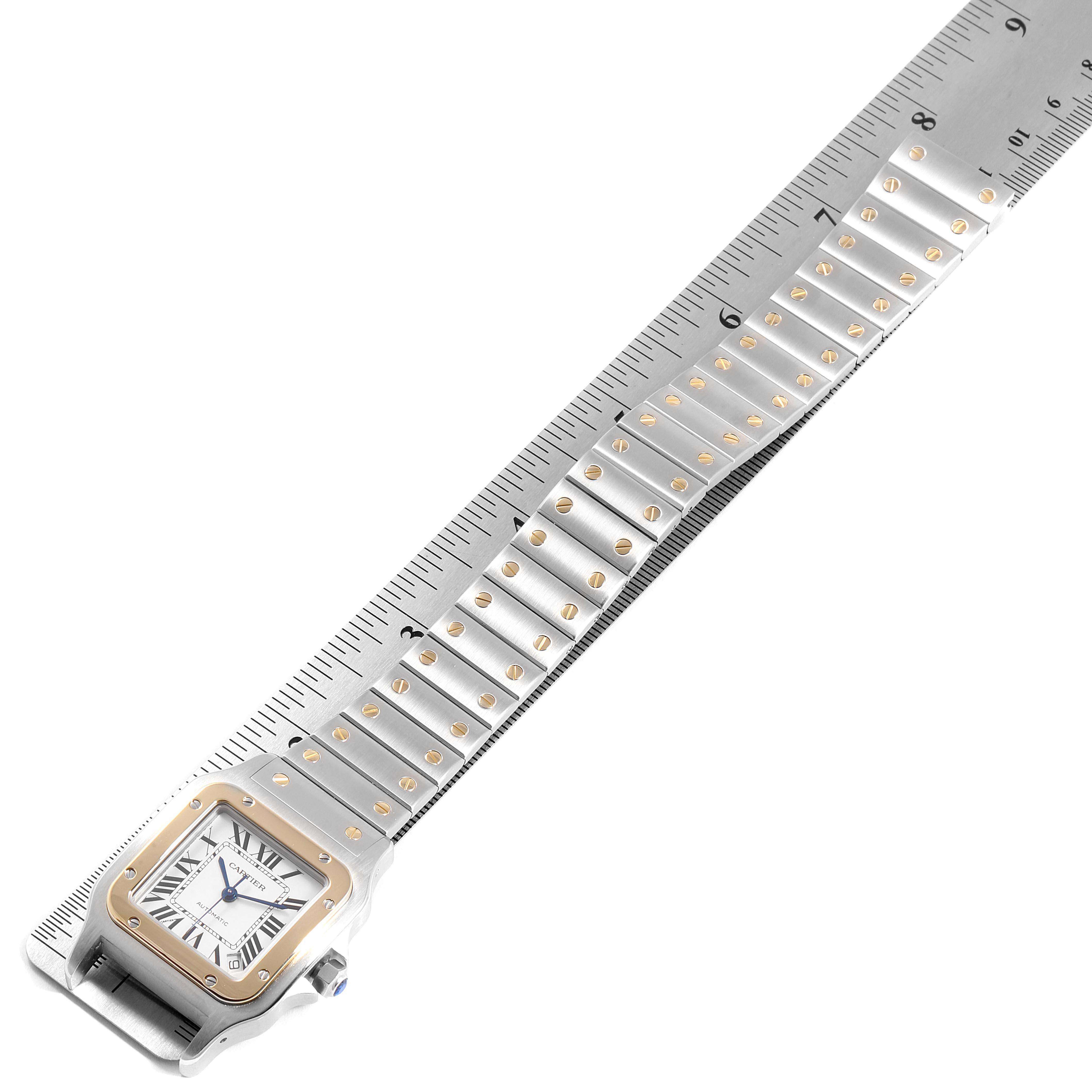 The image shows a Santos model by Cartier from an angled top view, displaying the watch face and bracelet resting on a ruler.