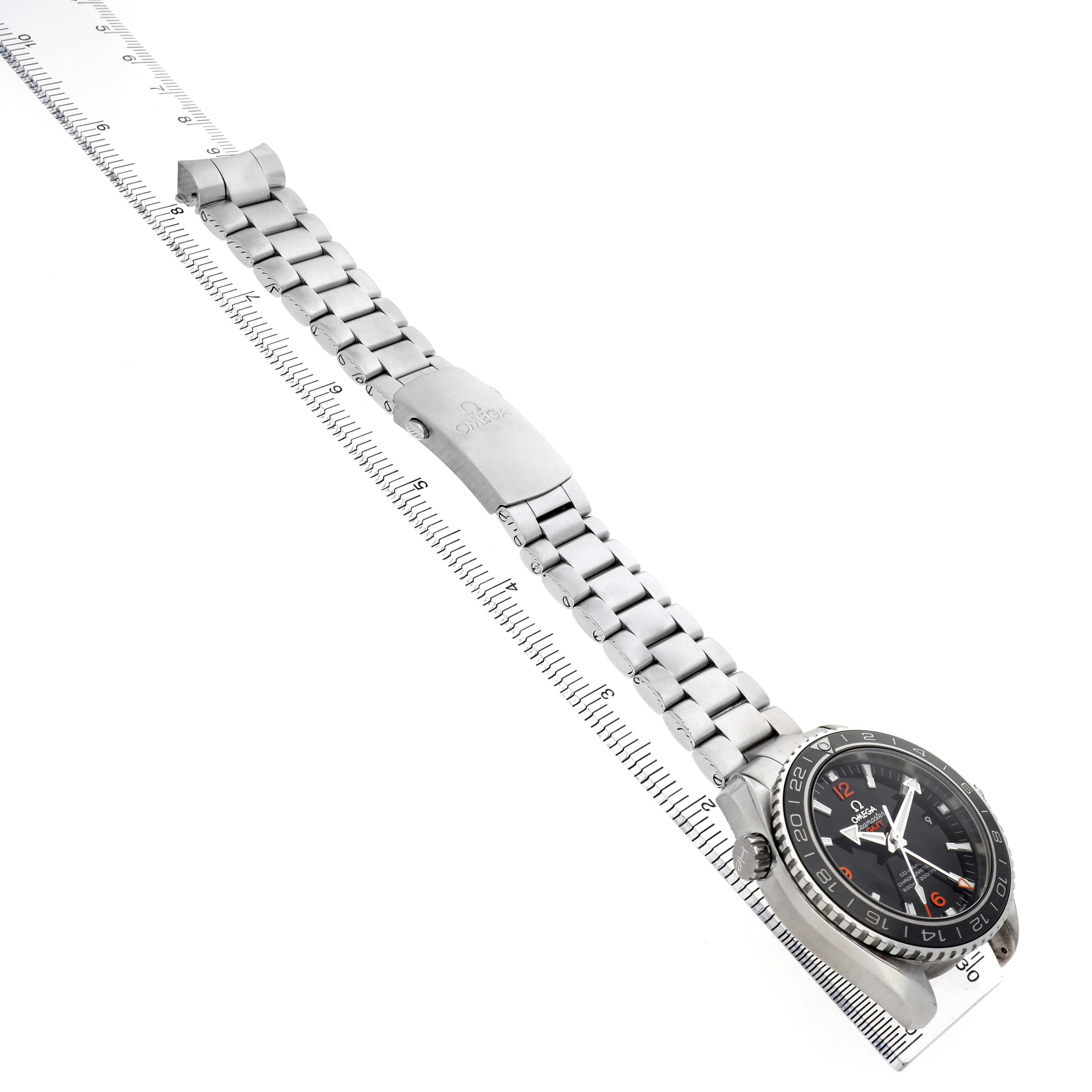The Omega Planet Ocean 232.30.44.22.01.002 Men's Stainless Steel Black Dial watch is shown at an angle displaying the face, bracelet, clasp, and part of the bezel on a ruler.