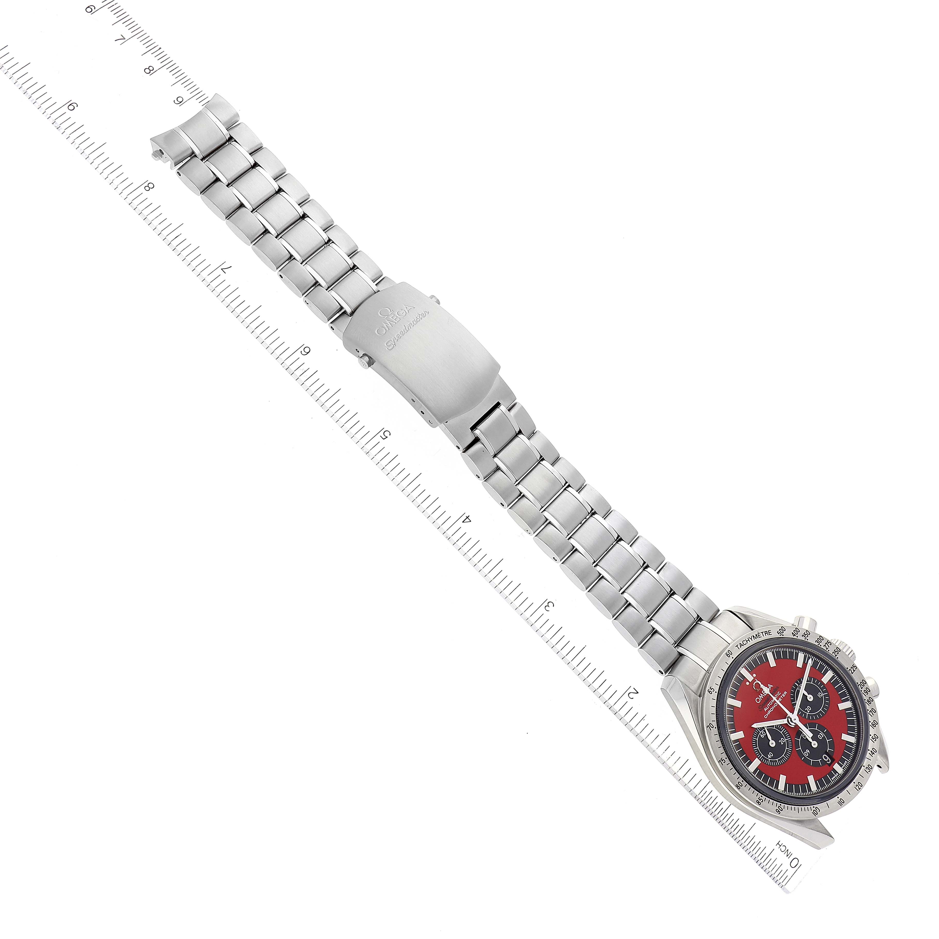 The image shows an Omega Speedmaster 3506.61.00 Men's Stainless Steel Red Dial 3506.61.00 Men's Stainless Steel Red Dial watch at a slight angle, highlighting its red dial and stainless steel bracelet laid next to a ruler.