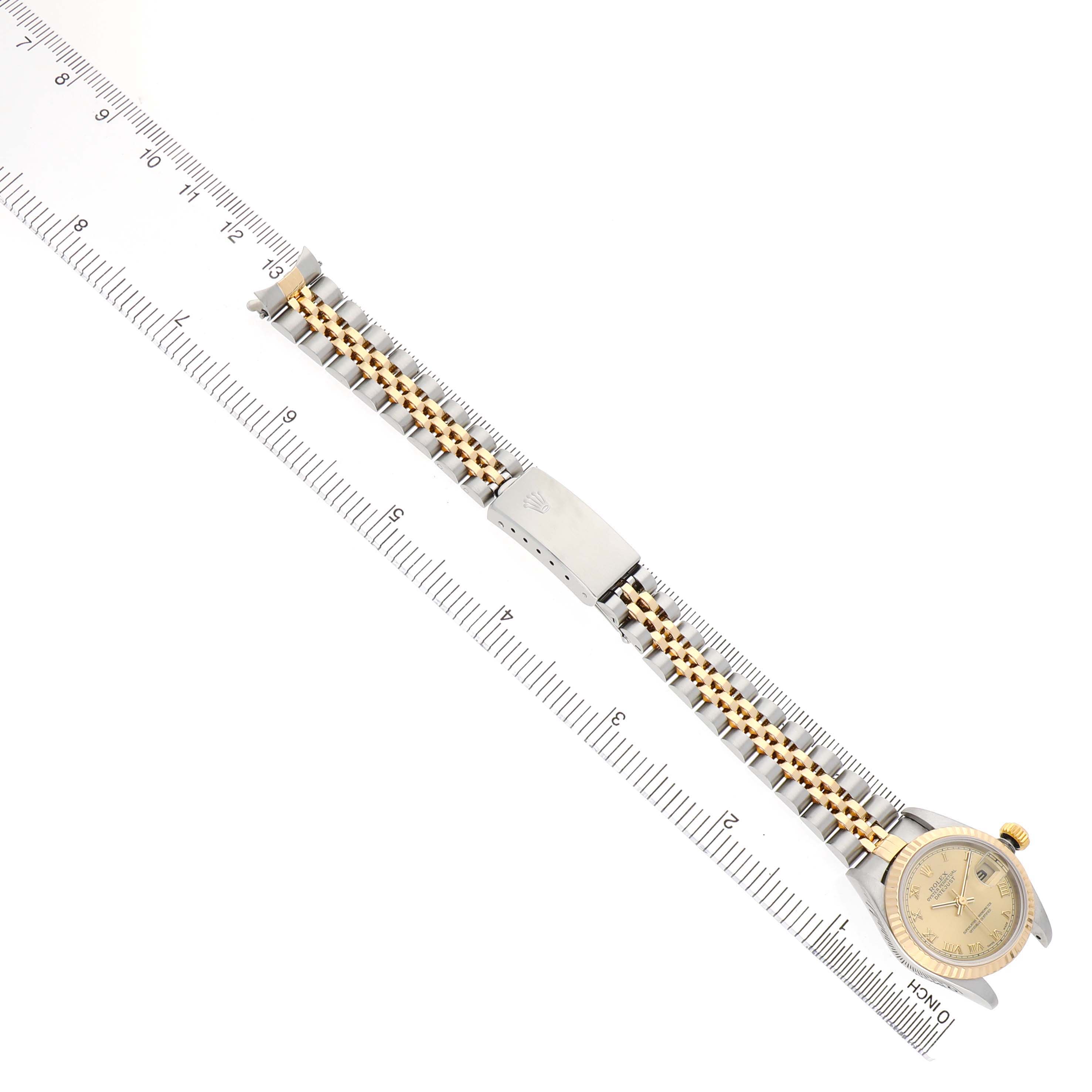The Rolex Datejust 79173 Women's Steel and Gold (two tone) Champagne Dial watch is shown from a top view, highlighting the bracelet, clasp, and face alongside a ruler.