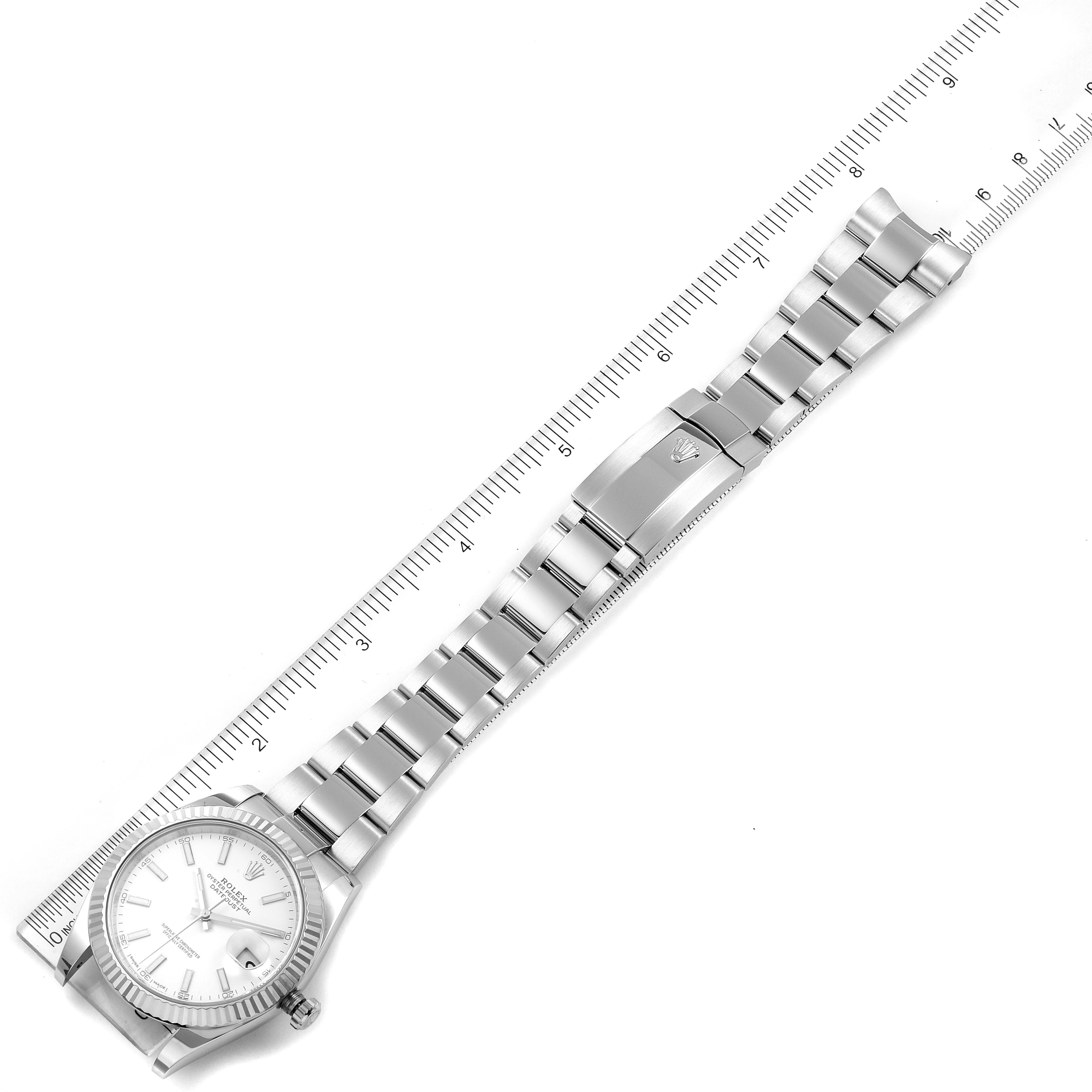 The image shows a top-down view of a Rolex Datejust 126334 Men's Stainless Steel White Dial 126334 Men's Stainless Steel White Dial watch, highlighting the watch face and full metal bracelet against a ruler.
