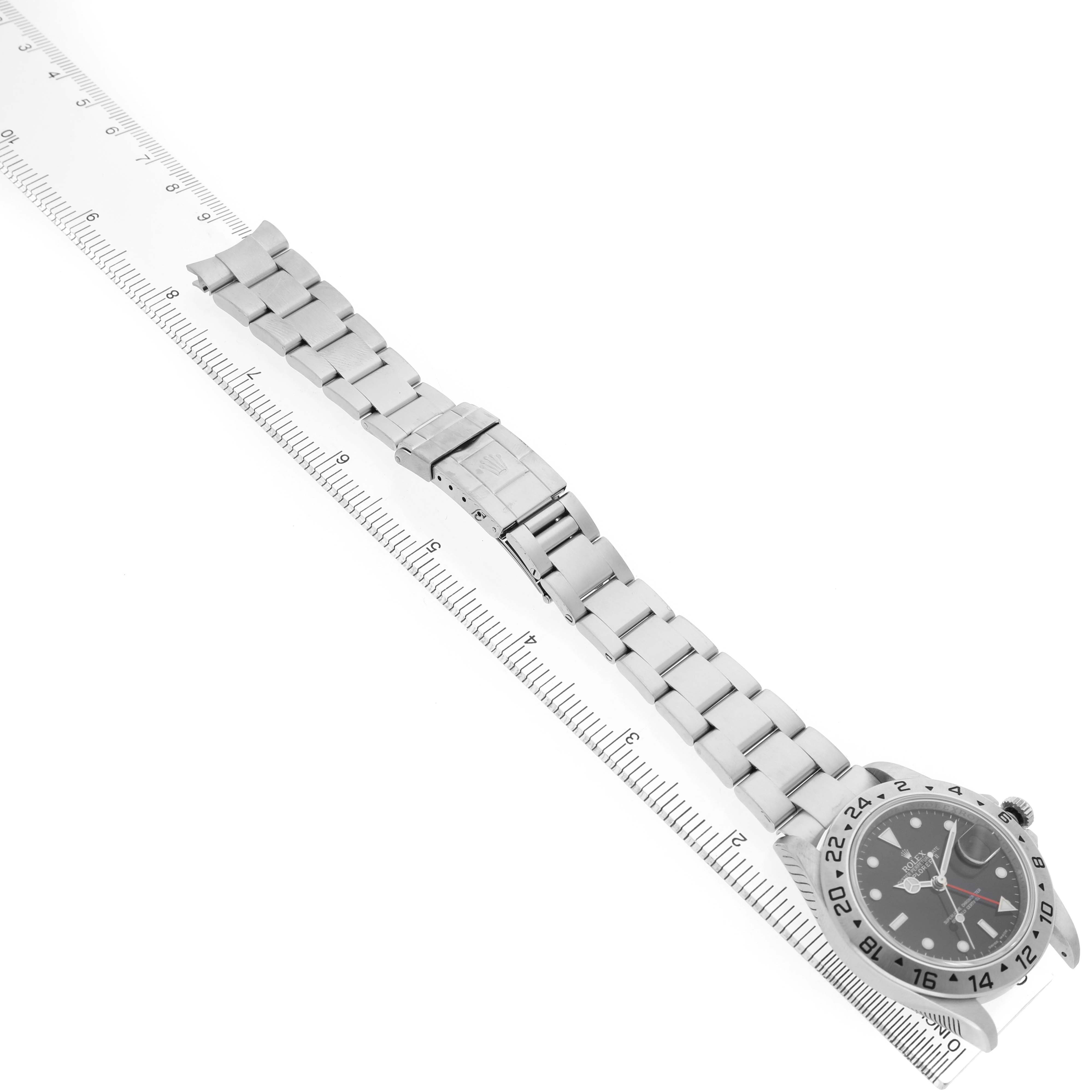The image shows a Rolex Explorer 16570 Men's Stainless Steel Black Dial watch from a top view, displaying the full band, clasp, and face alongside a ruler for scale.