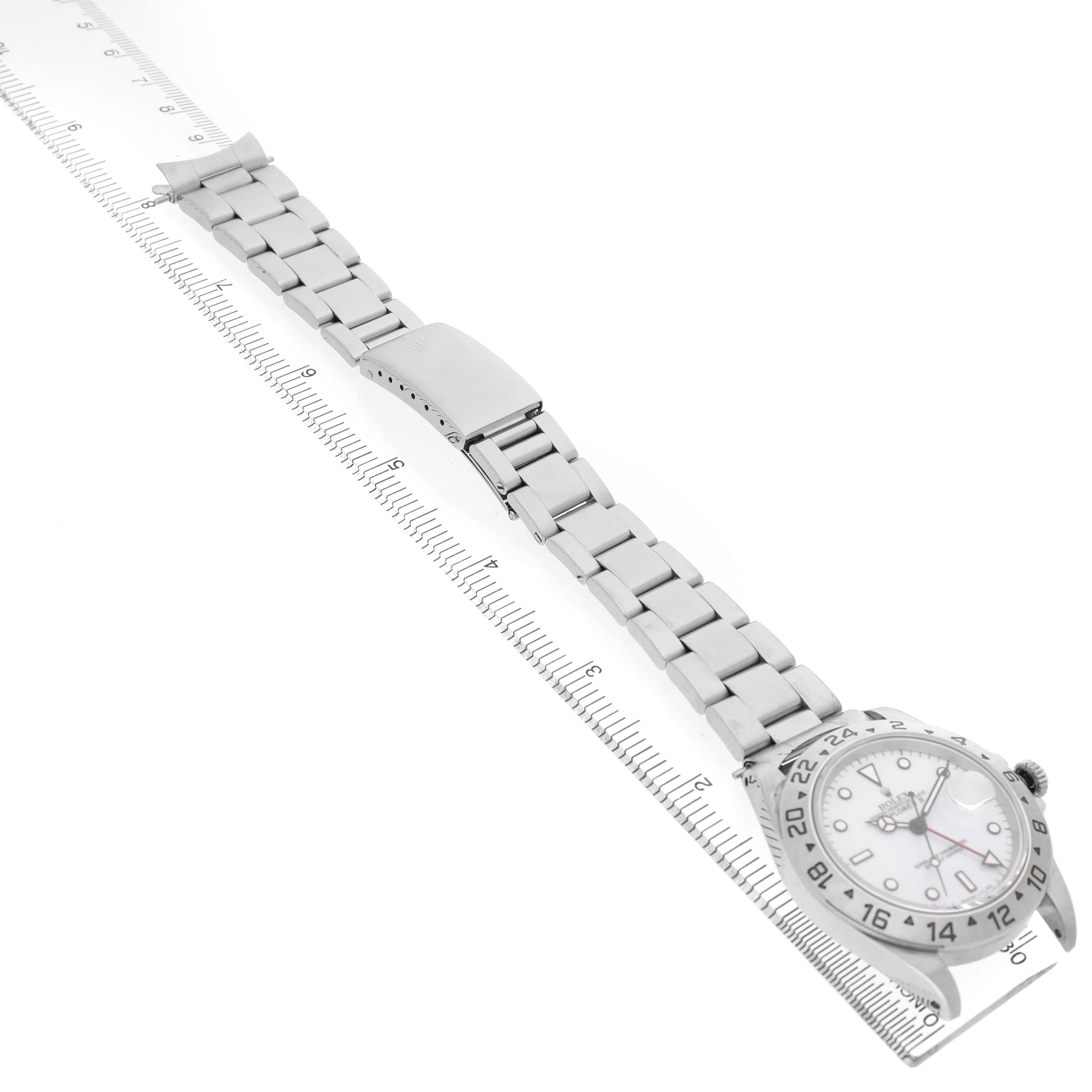 The Rolex Explorer 16570 Men's Stainless Steel White Dial watch is shown laid flat, displaying the bracelet and face alongside a ruler for scale.