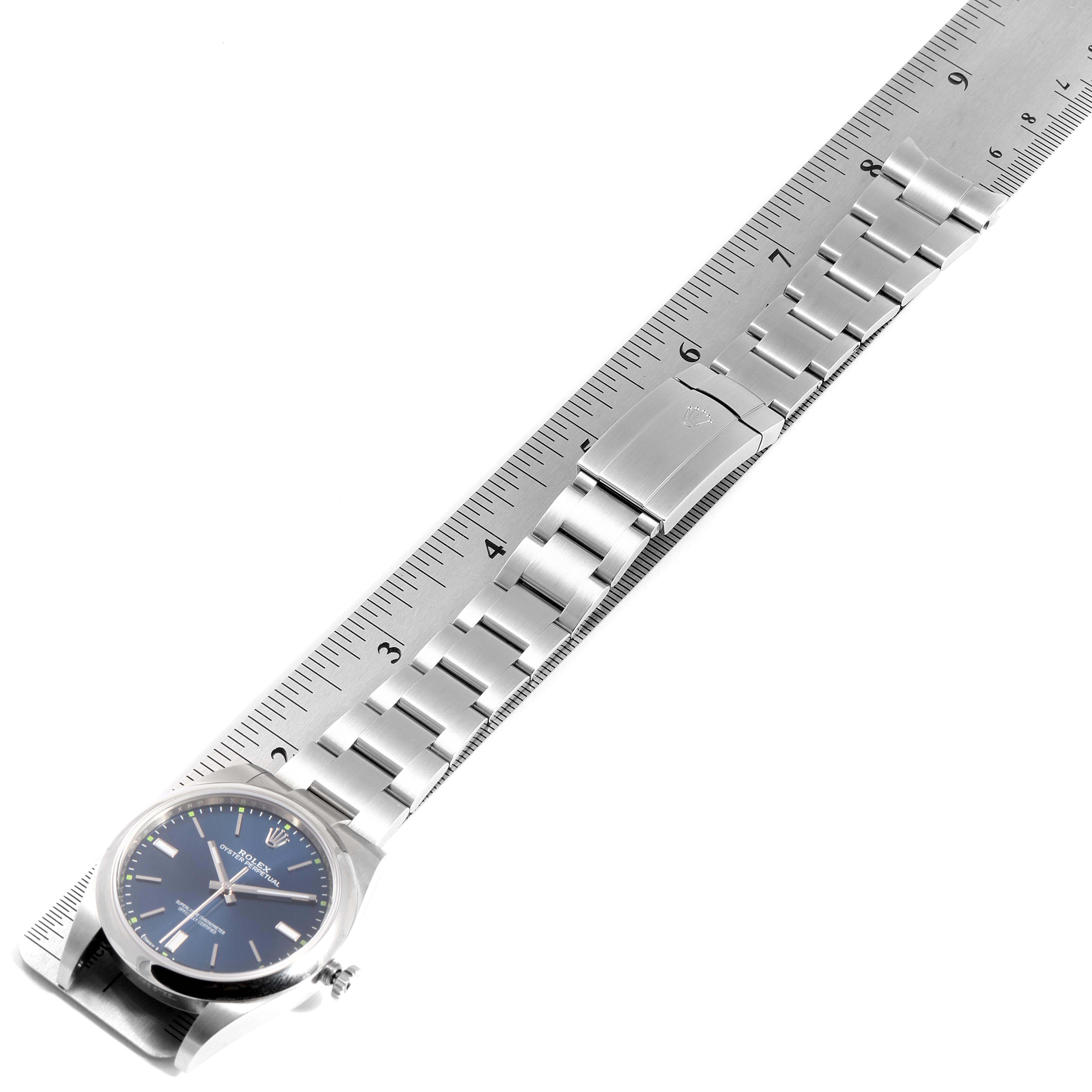 The image shows the entire Rolex Oyster Perpetual 114300 Men's Stainless Steel Blue Dial 114300 Men's Stainless Steel Blue Dial watch, including the face, case, and metal bracelet on a ruler.