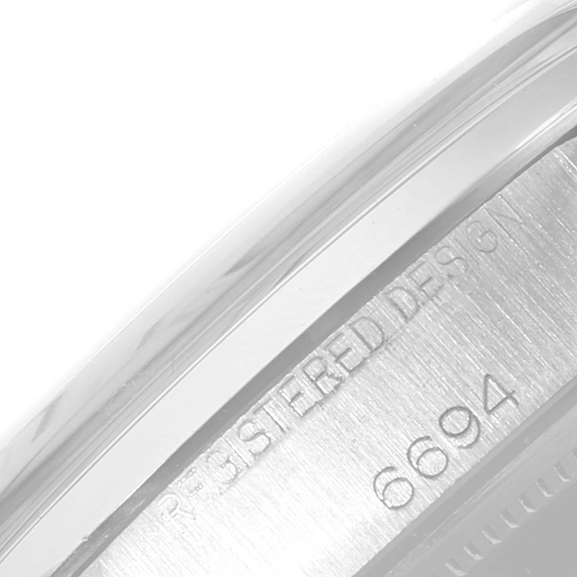 The image shows a close-up of the side of a Rolex Vintage Collection 6694 Men's Stainless Steel Silver Dial 6694 Men's Stainless Steel Silver Dial watch, focusing on the engraved serial number and "REGISTERED DESIGN."