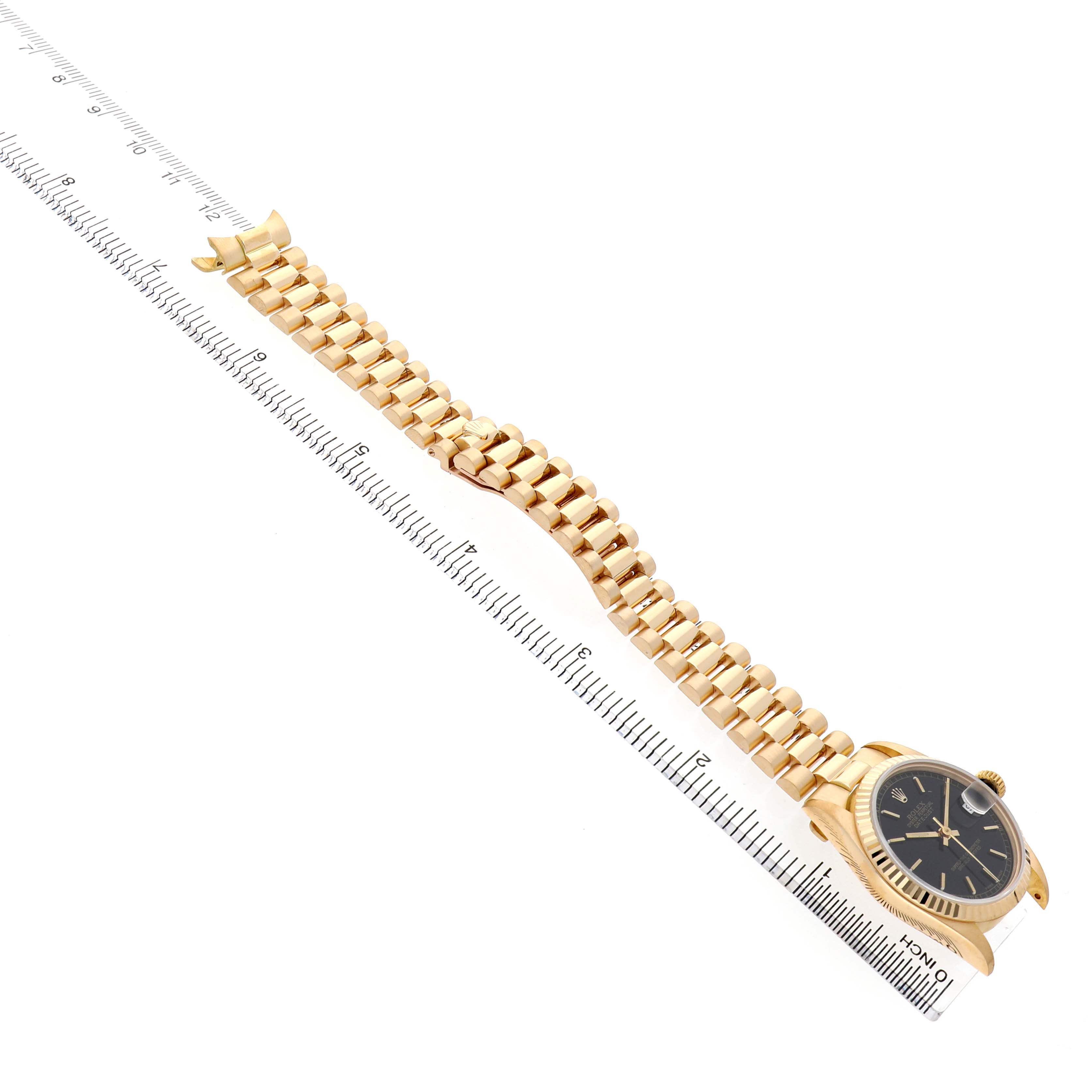 The Rolex President 68278 Women's Yellow Gold Black Dial watch is shown from an angled top view, displaying its gold bracelet and black dial alongside a ruler.