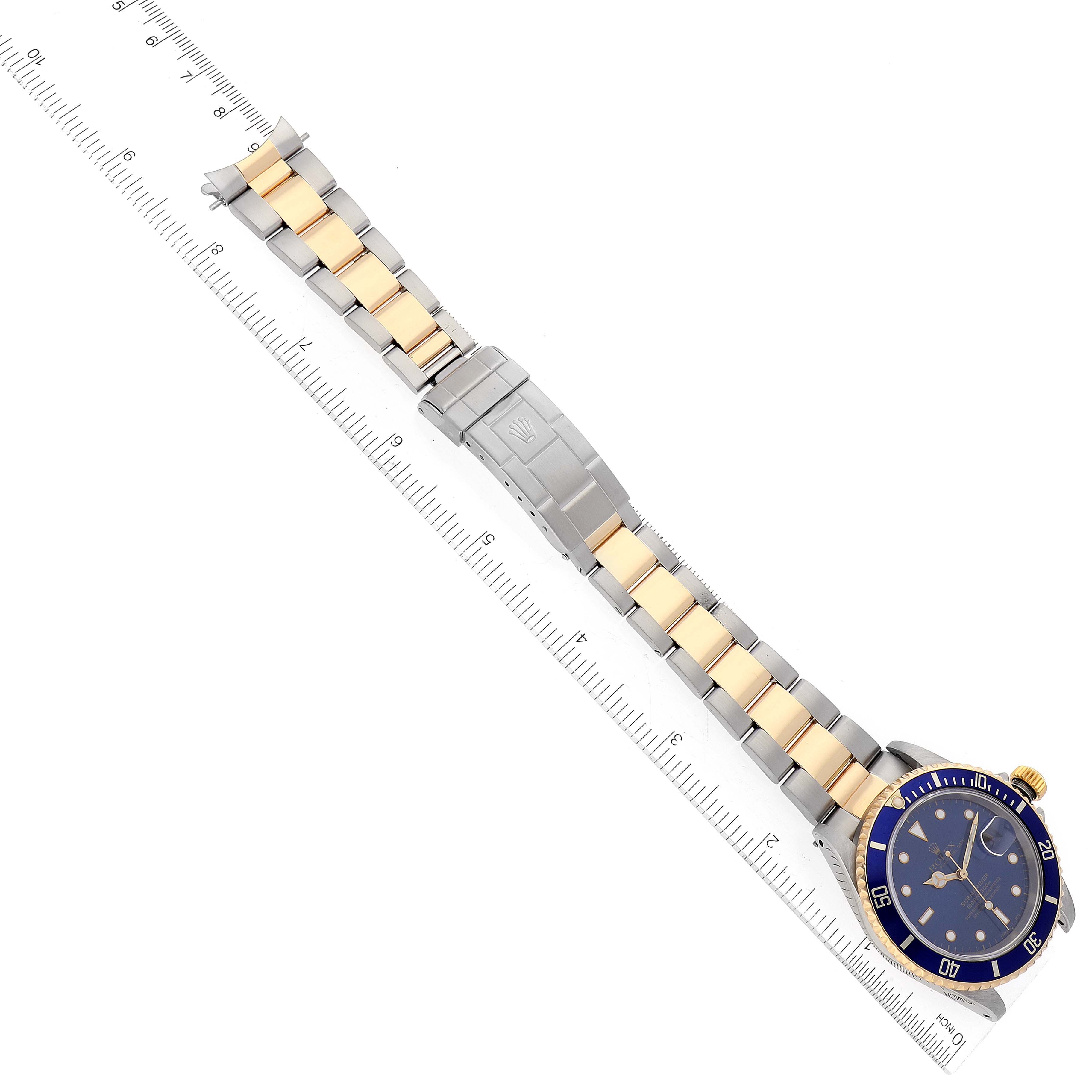 The image shows a Rolex Submariner 16613 Men's Steel and Gold (two tone) Blue Dial 16613 Men's Steel and Gold (two tone) Blue Dial watch laid flat, with its stainless steel and gold bracelet fully extended alongside a ruler.