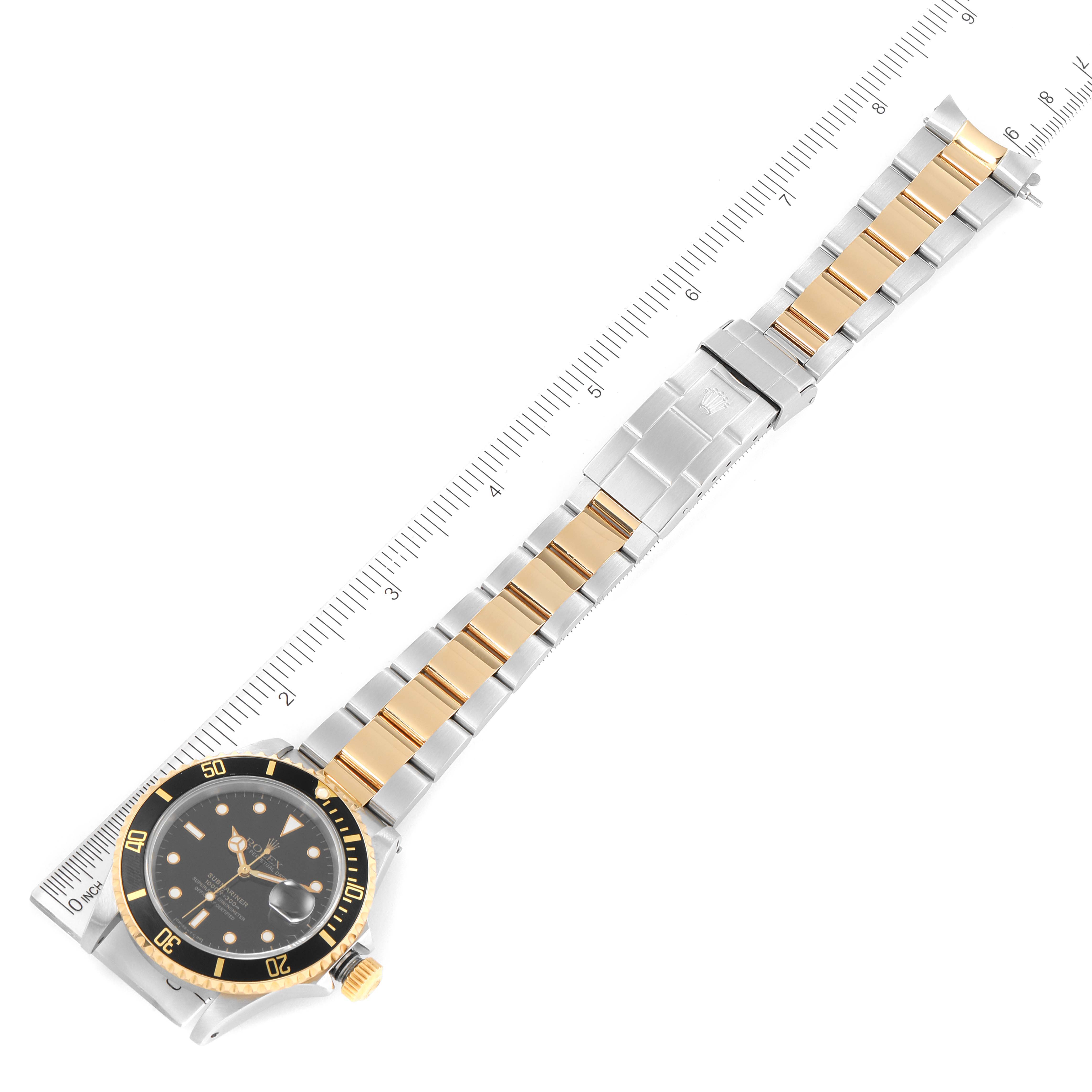 The image shows a Rolex Submariner 16613 Men's Steel and Gold (two tone) Black Dial 16613 Men's Steel and Gold (two tone) Black Dial watch laid flat with its face, band, and clasp visible, alongside a ruler for measurement.