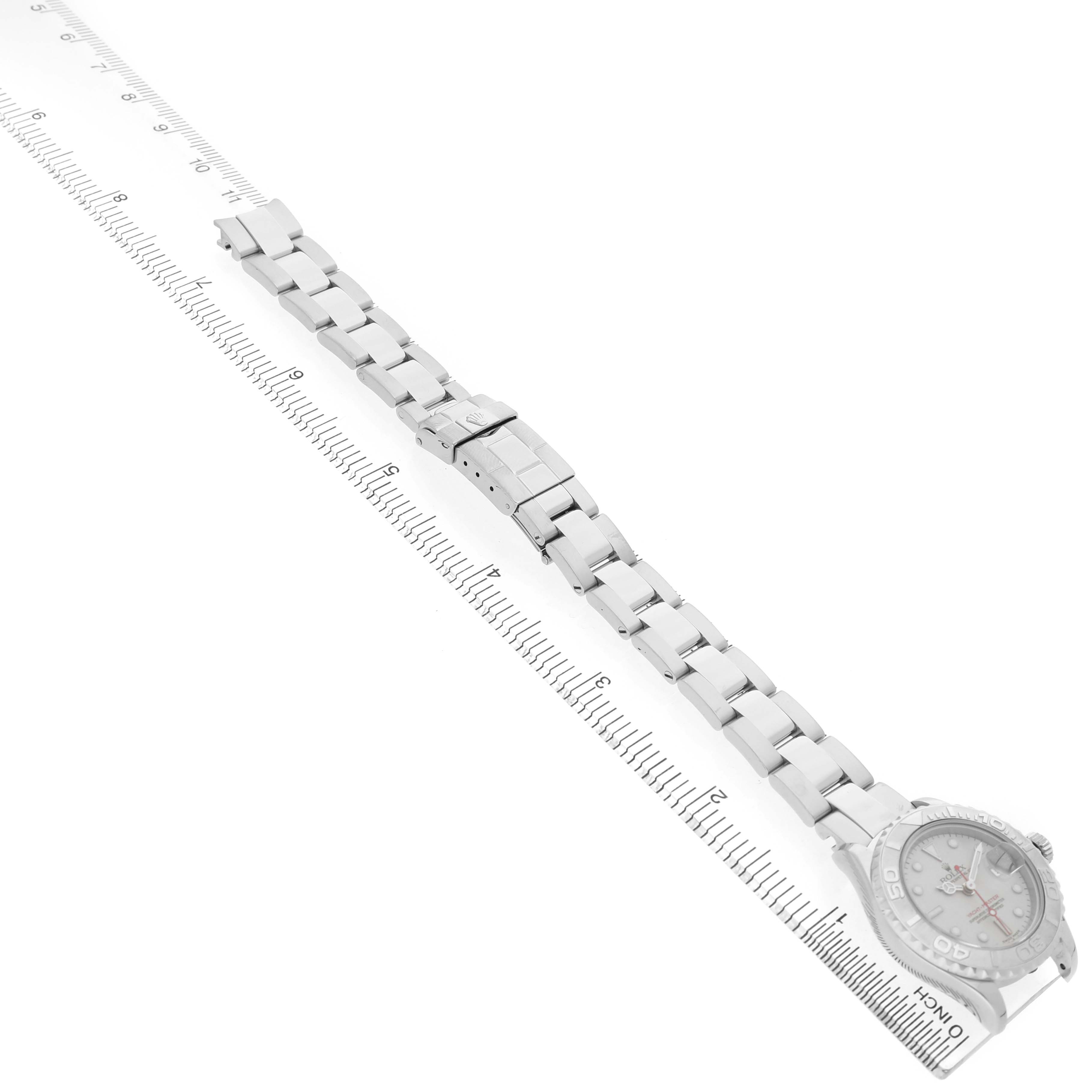 The Rolex Yacht-Master 169622 Women's Stainless Steel Silver Dial watch is shown from an overhead angle, displaying the watch face, bracelet, and clasp, with a ruler beside it.