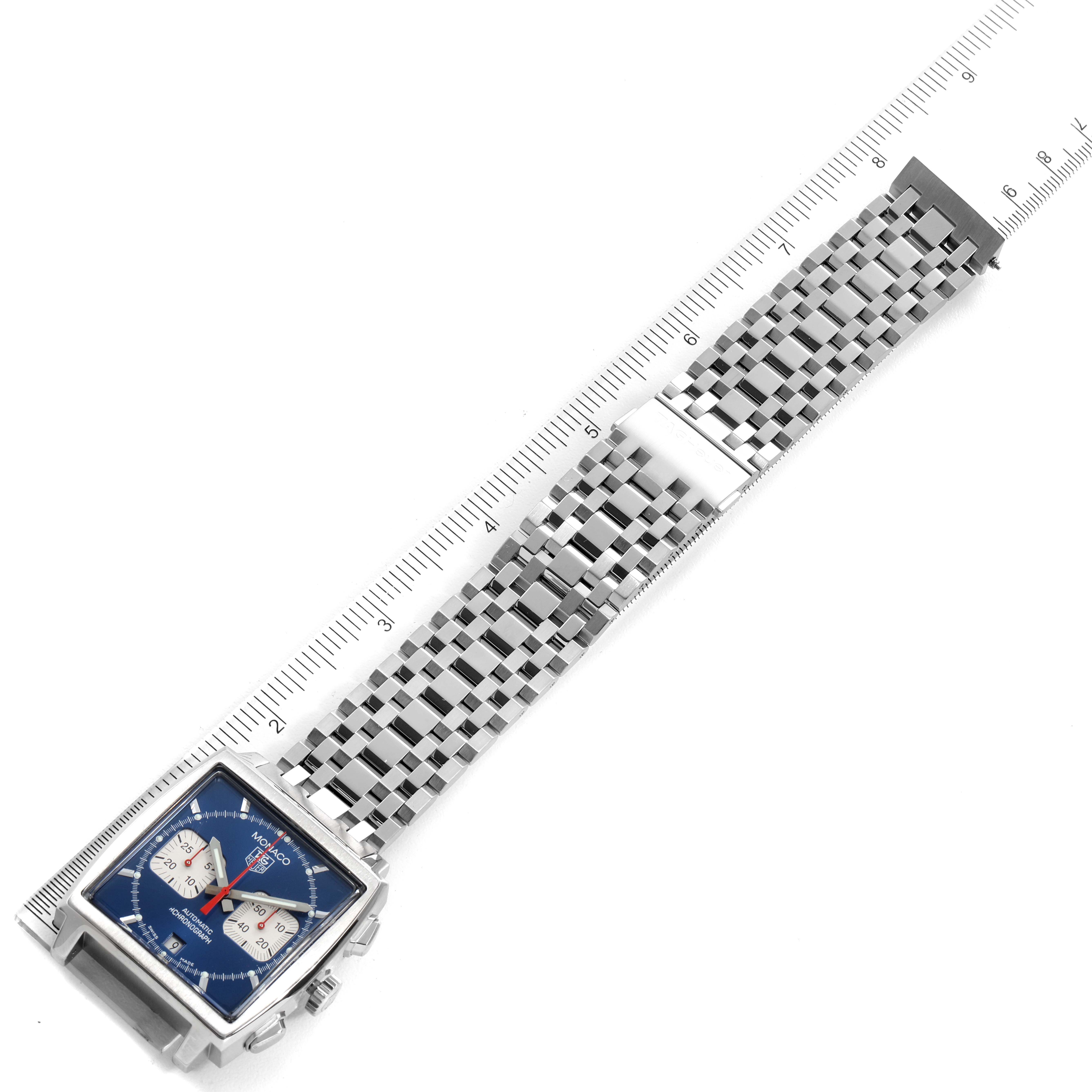 The image shows a Tag Heuer Monaco CW2113.BA0780 Men's Stainless Steel Blue Dial CW2113.BA0780 Men's Stainless Steel Blue Dial watch lying flat, with its square face and stainless steel bracelet visible, alongside a ruler for measurement.