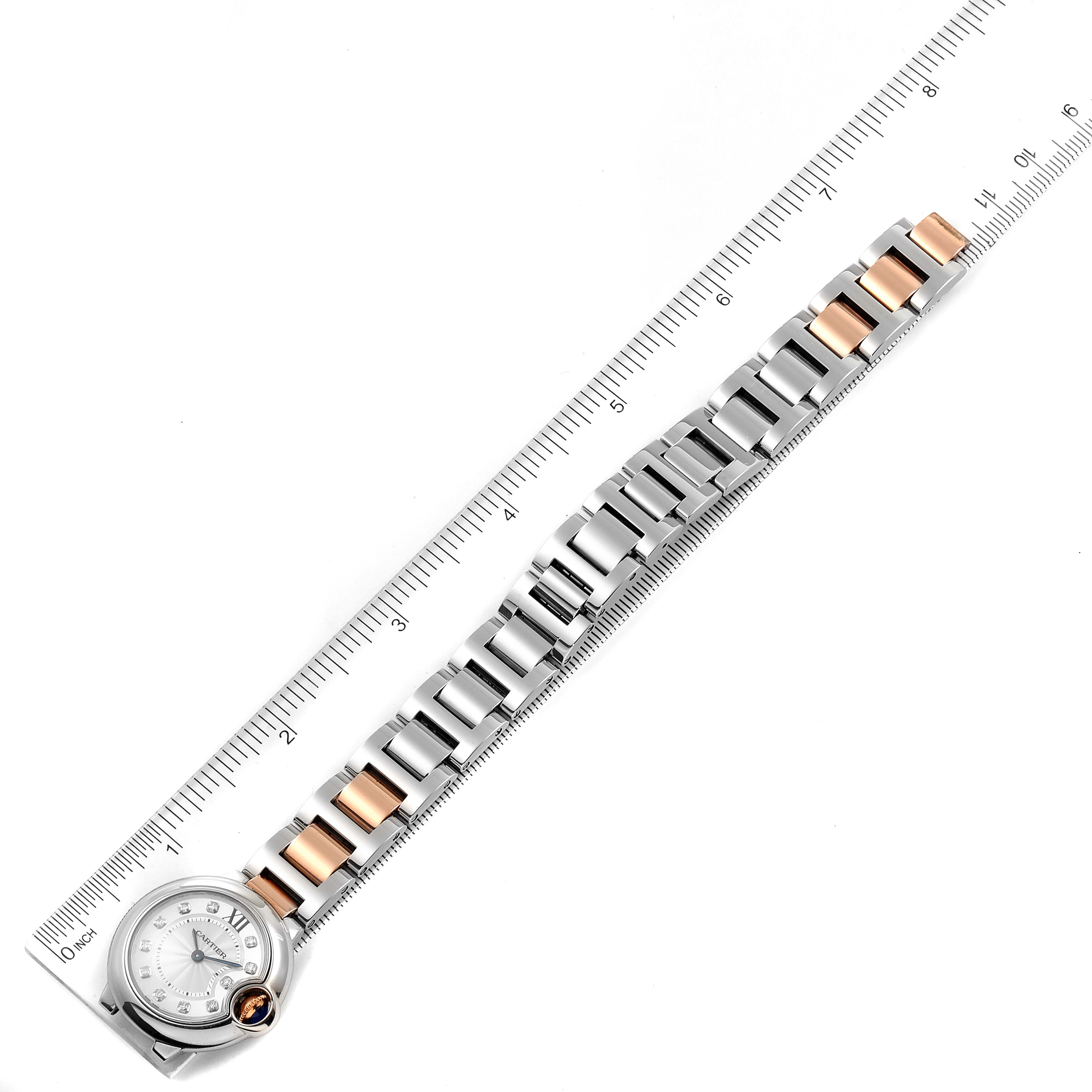 The image shows the Cartier Ballon Bleu WE902030 Women's Steel and Gold (two tone) Silver Dial WE902030 Women's Steel and Gold (two tone) Silver Dial watch laid flat next to a ruler, highlighting its metal bracelet and face.