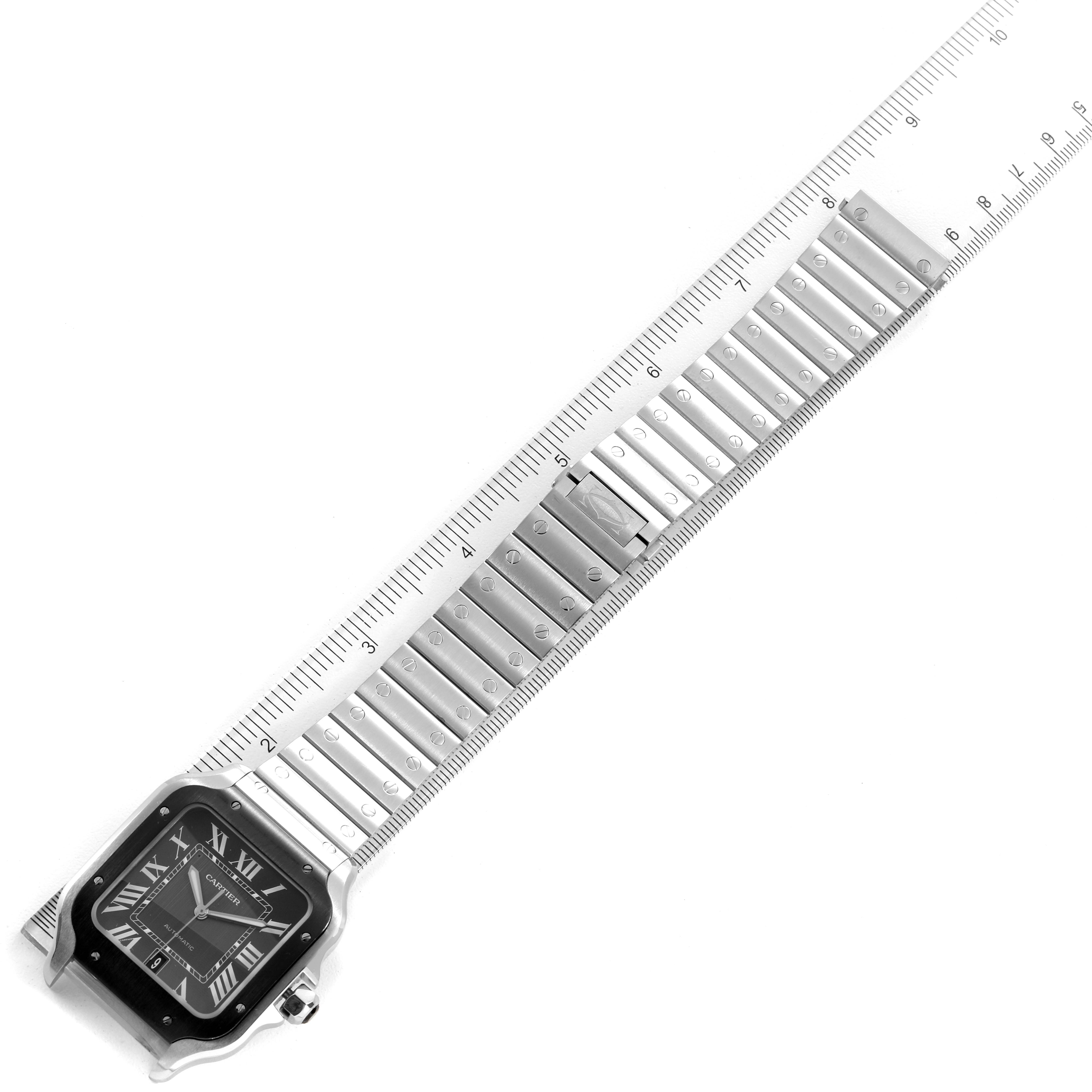 The Santos model watch by Cartier is shown diagonally, displaying the face and metal bracelet alongside a ruler for measurement.