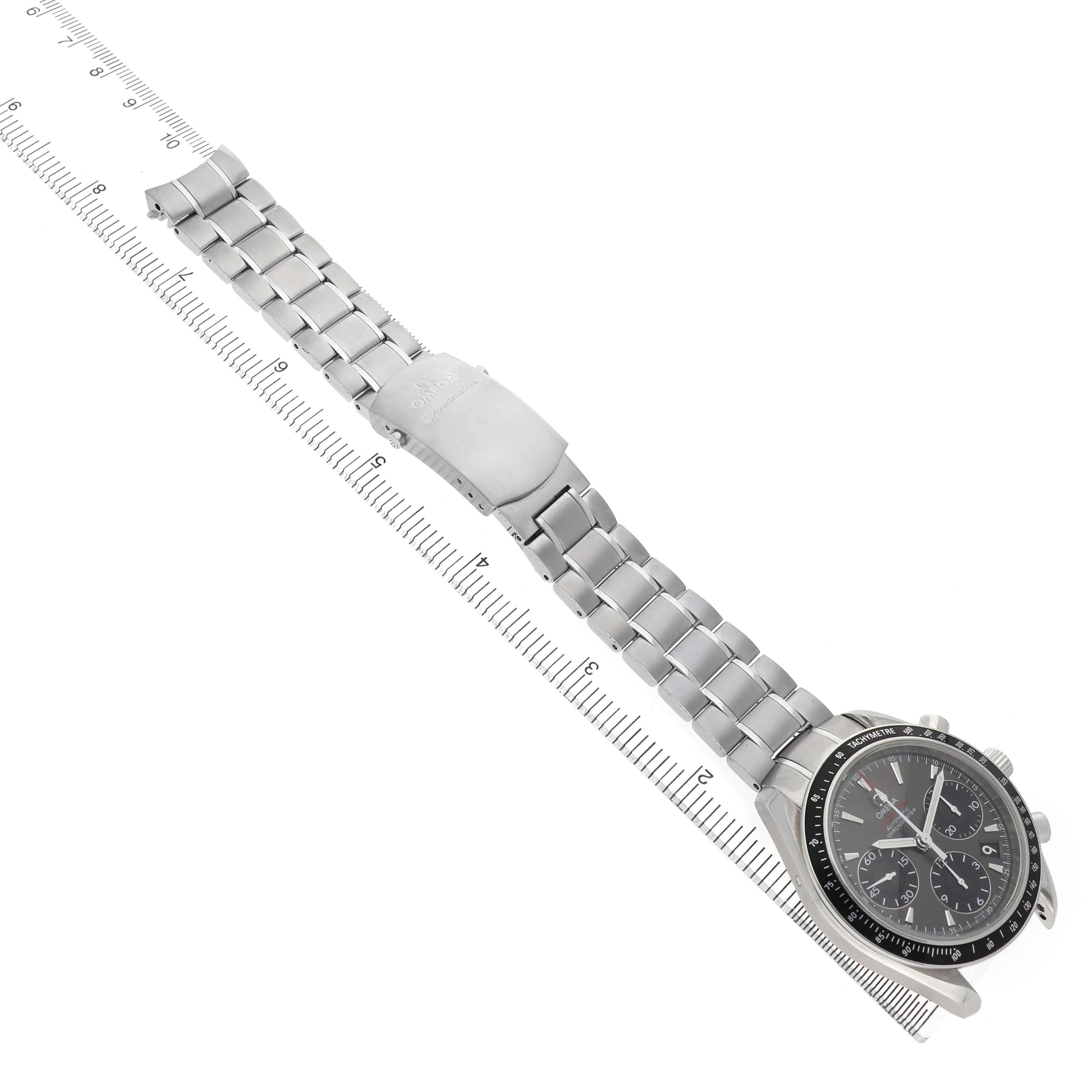The Omega Speedmaster 323.30.40.40.06.001 Men's Stainless Steel Grey Dial watch is shown diagonally with the bracelet extended and the clasp visible, alongside a measuring tool.